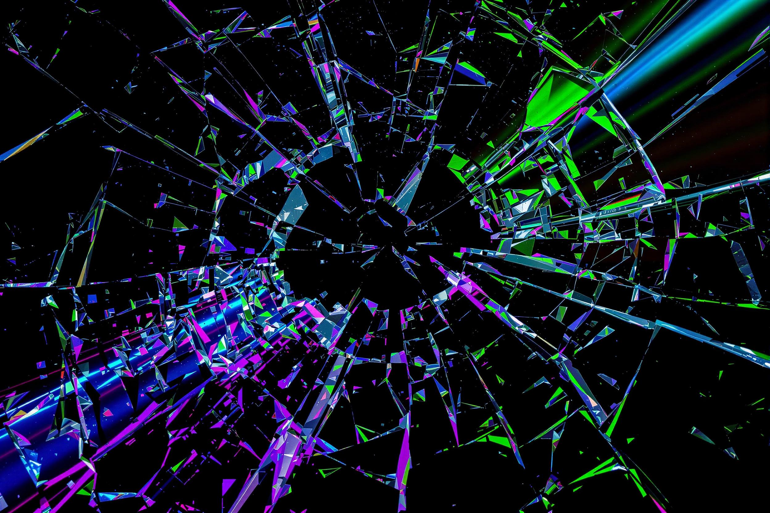 An extreme close-up showcases an abstract composition of shattered glass fragments on a smooth black background. Vibrant beams of purple, green, and blue light refract strikingly through the shards, creating intricate patterns and sharp contrasts. Defined edges and reflective surfaces highlight the texture, forming a dynamic interplay between chaos and clarity.