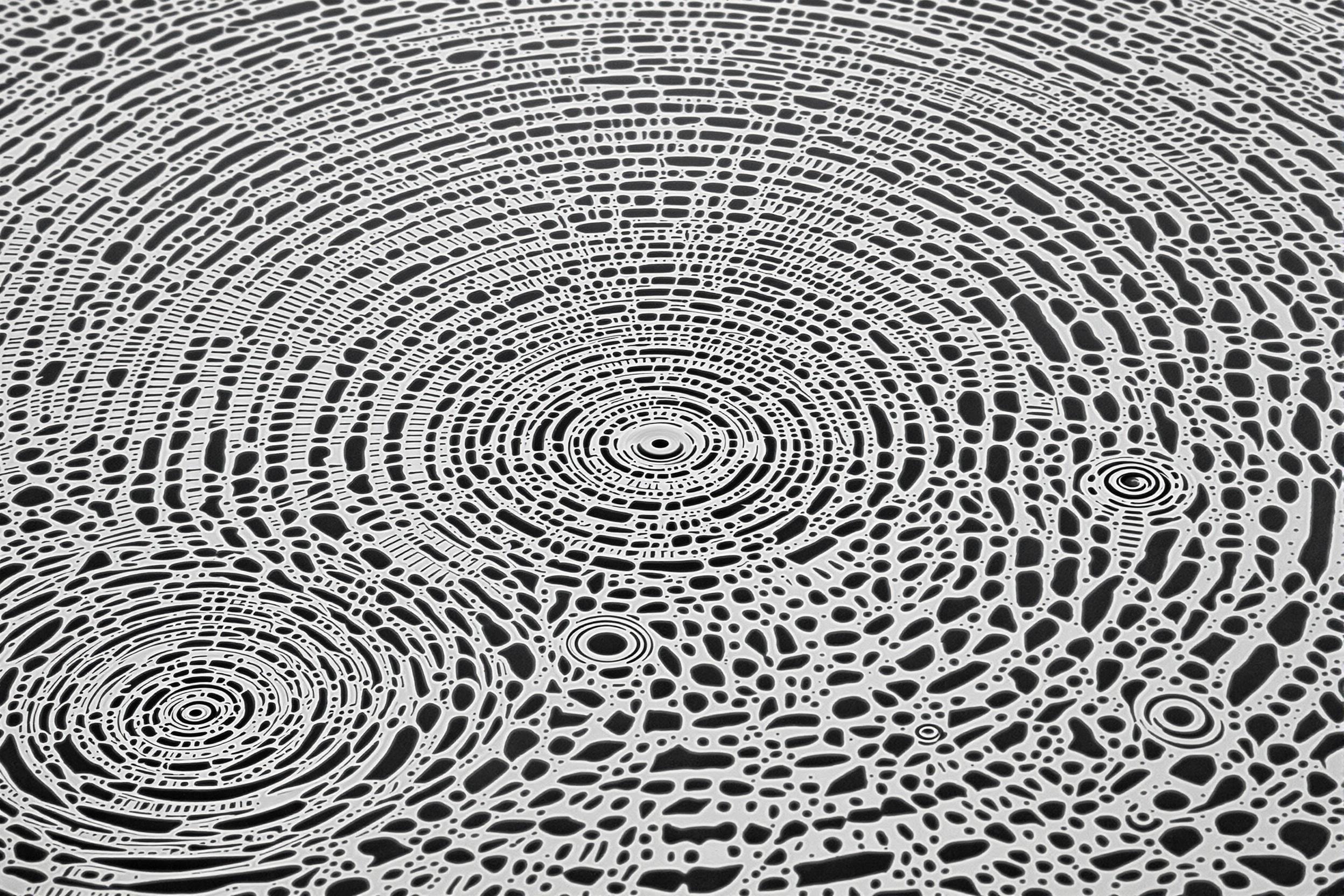 Mesmerizing abstract photograph capturing the intricate patterns of water ripples. Concentric circles and intersecting waves create a hypnotic composition, showcasing nature's inherent artistry. Soft, monochromatic palette emphasizes form and texture.