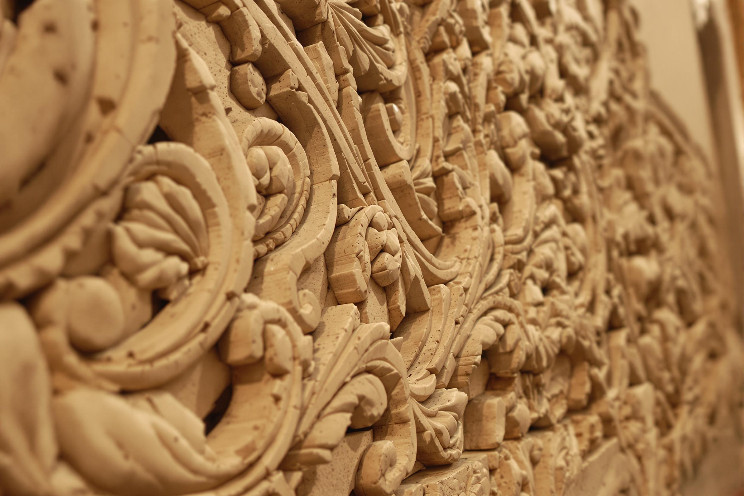 A close-up depicts ornate ancient stone relief carvings rendered with breathtaking detail. The texture reveals weathering over time, with faint tool marks and graceful patterns etched into the stone. Warm diffused indoor light highlights every groove and contour, casting subtle shadows that augment depth.