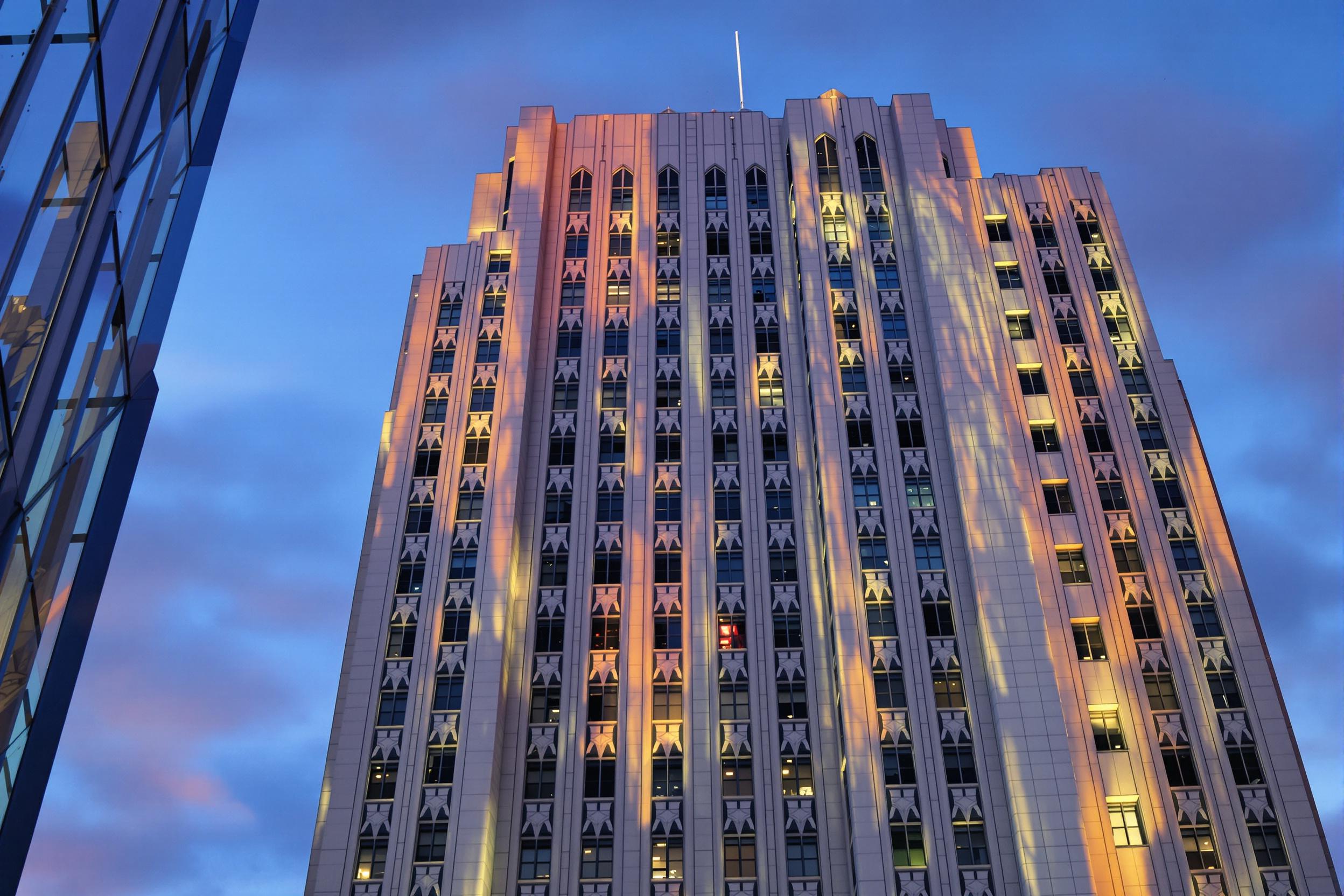 Capture the timeless elegance of Art Deco architecture as twilight descends on a majestic skyscraper. Sharp geometric patterns cast dramatic shadows across the facade, creating a mesmerizing interplay of light and form.