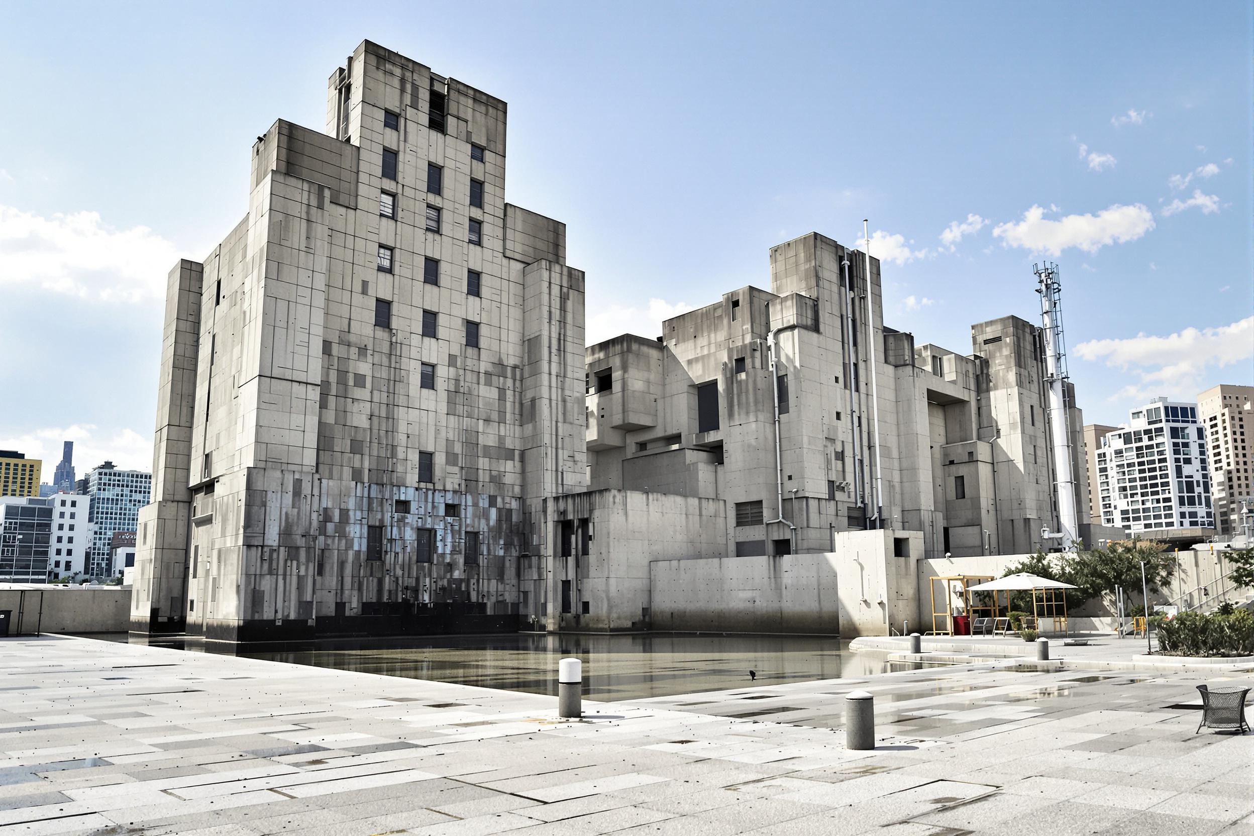 Explore the raw beauty of industrial architecture in this striking image of a brutalist water treatment facility. Massive concrete forms create a sculptural silhouette against an urban skyline, showcasing the intersection of form and function in municipal infrastructure.