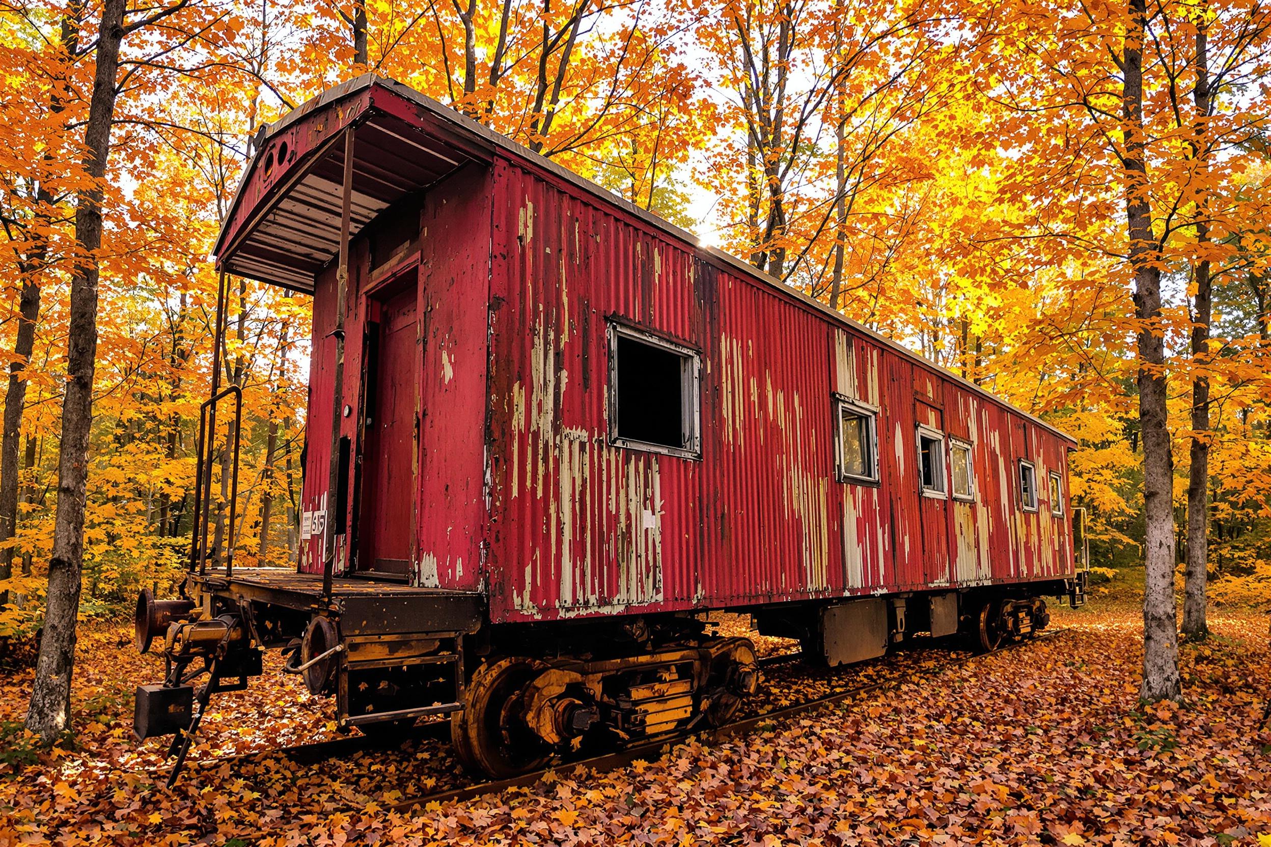 A weathered, vintage train caboose rests abandoned amidst a colorful autumn forest. Rusted siding with faded red paint contrasts beautifully against vibrant orange and yellow foliage. Golden-hour sunlight filters through tree branches, adding a soft glow that accentuates the textured metal exterior and scattered dry leaves lining the ground.