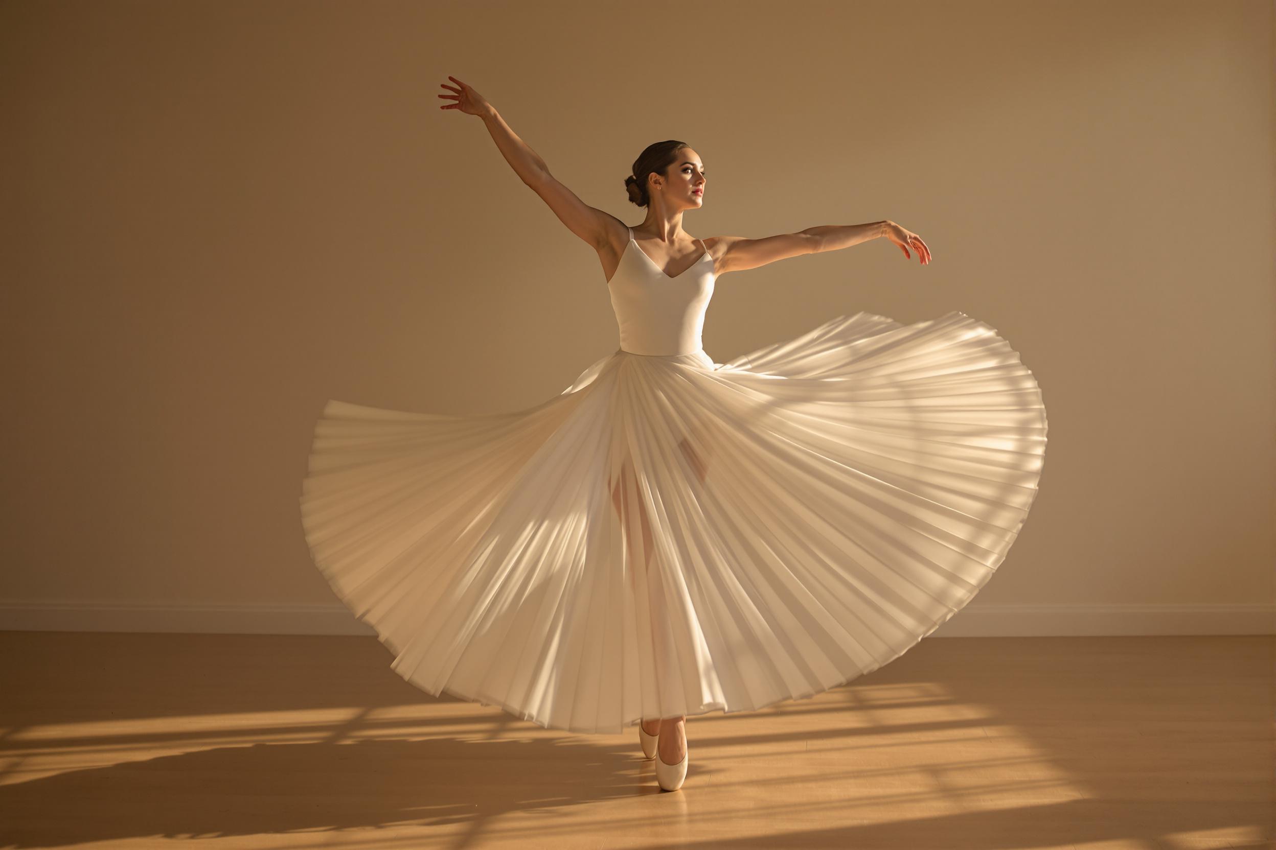 An artistic portrait captures a ballerina mid-twirl in a softly lit studio. Her flowing white dress cascades around her, creating graceful curves against the polished wooden floor. Bathed in warm late afternoon light, the dancer's concentrated expression highlights her dedication as her arms extend elegantly. The background fades away gently, emphasizing the elegance of her motion and form.