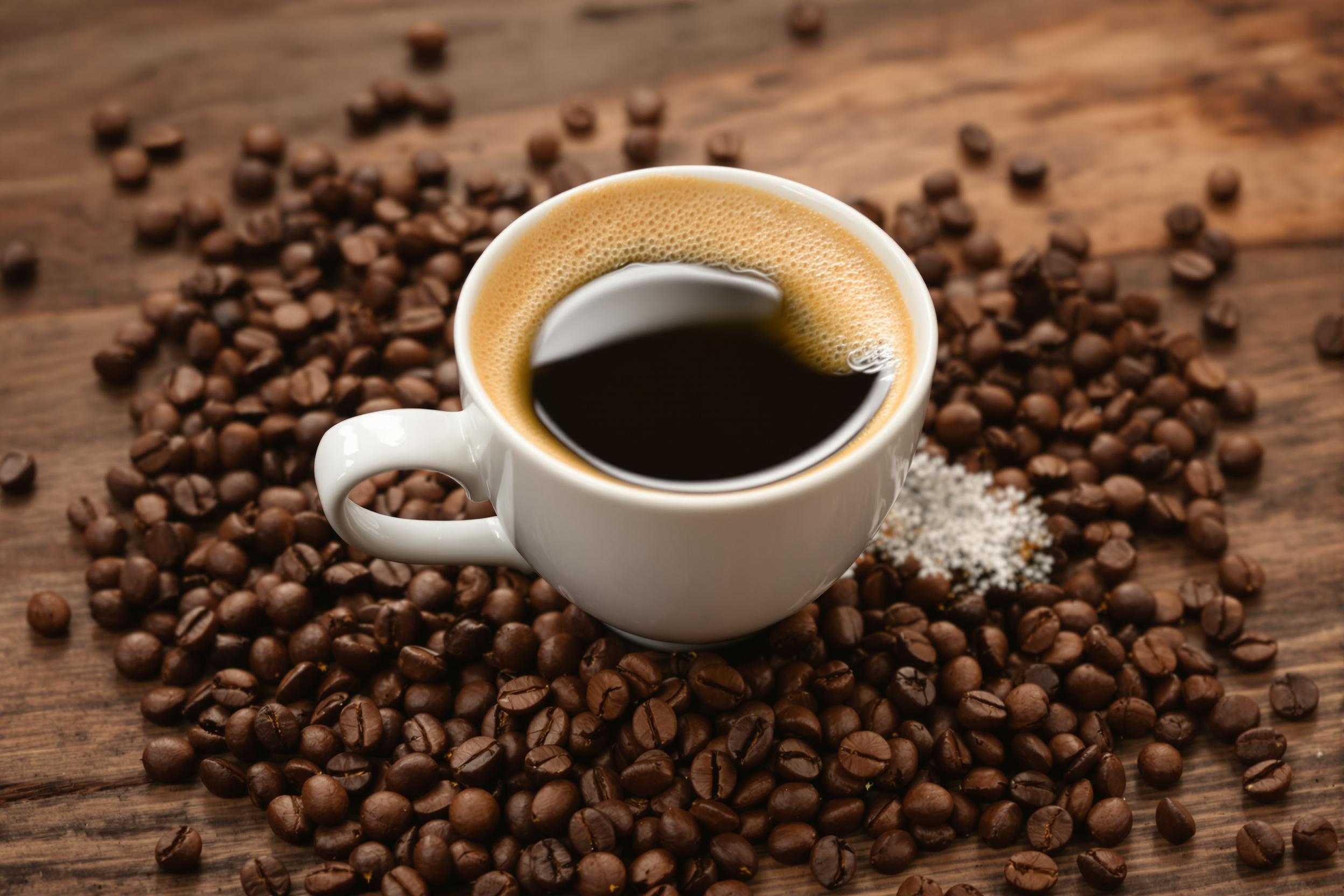 A close-up captures a freshly brewed espresso served in a delicate white porcelain cup placed on a rustic wooden coffee table. The rich, dark liquid creates a velvety surface crowned with creamy froth, reflecting soft light. Surrounding the cup, a scattering of coffee beans adds texture and warmth to the scene. This intimate setup invites appreciation for the craftsmanship of coffee-making and evokes sensations of comfort and indulgence.