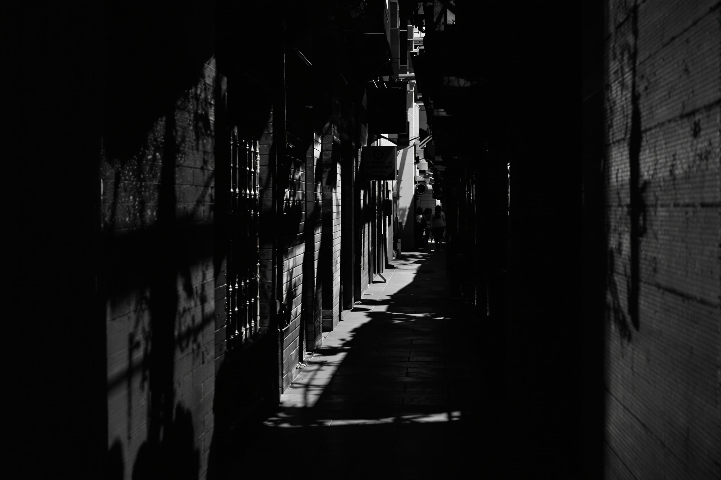 Explore the dramatic interplay of light and shadow in this experimental urban photograph. A narrow alleyway becomes a canvas for chiaroscuro, with stark contrasts creating a compelling visual narrative of city life.