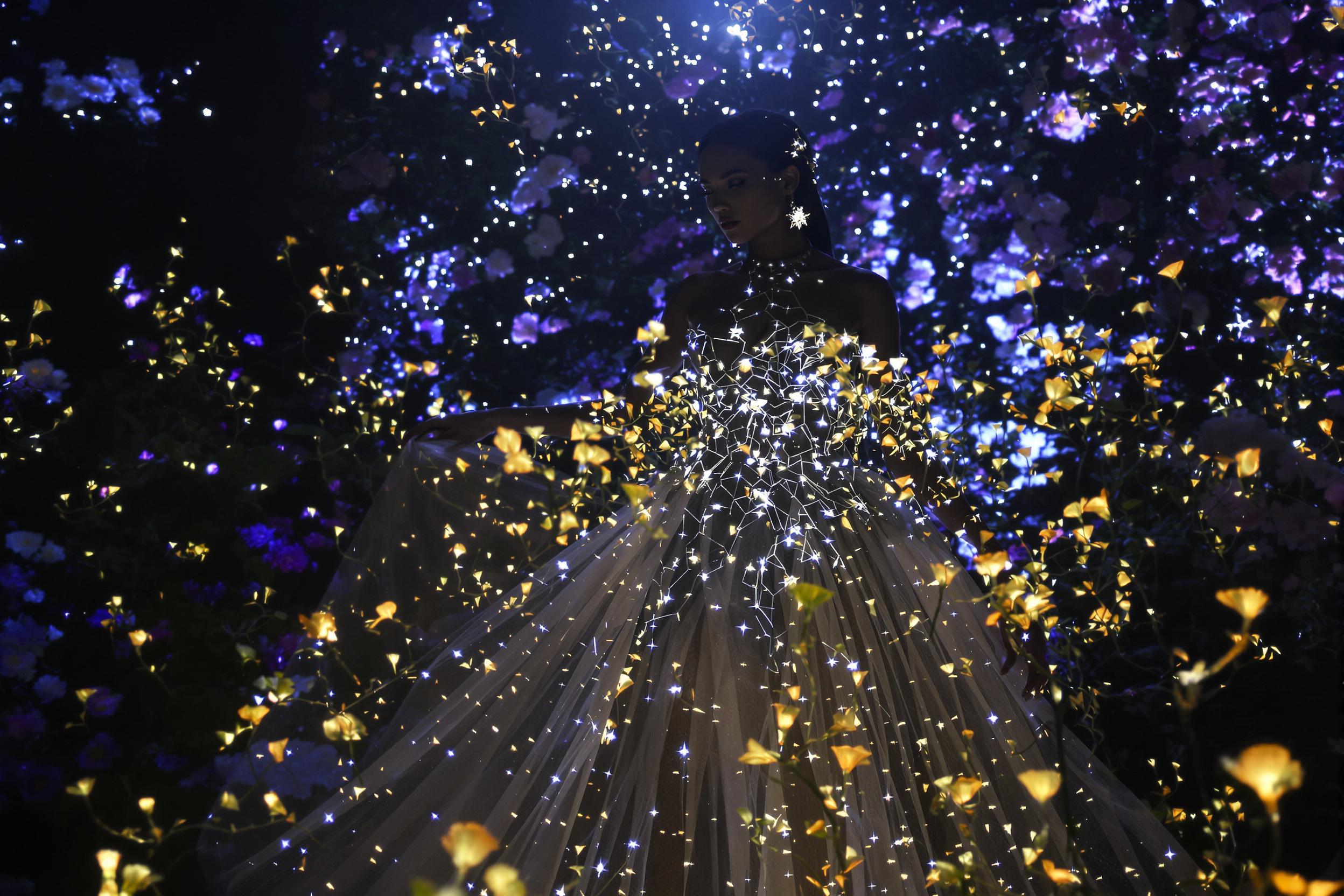 A breathtaking fusion of haute couture and celestial wonder unfolds in a moonlit garden. A model adorned in a gossamer gown embellished with twinkling LED constellations stands amidst bioluminescent flowers, creating a mesmerizing tableau of earthly and cosmic beauty.