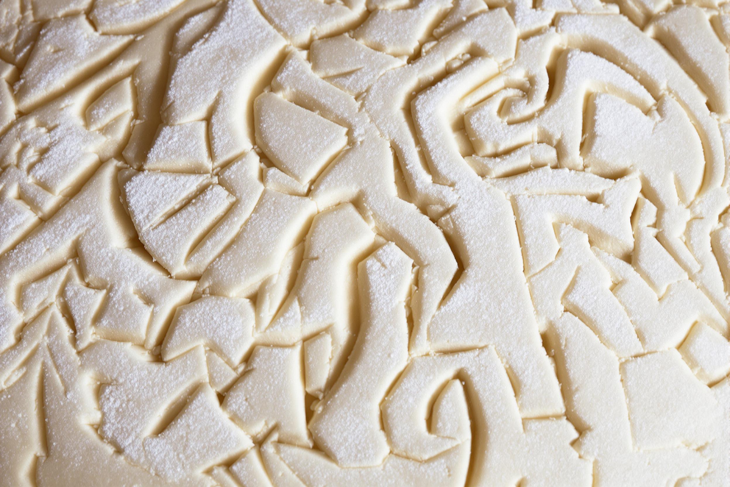 Close-up of intricately scored sourdough bread dough, showcasing various artistic patterns before baking. The pale, flour-dusted surface highlights the depth and precision of the cuts, emphasizing the craftsmanship in artisanal bread making.