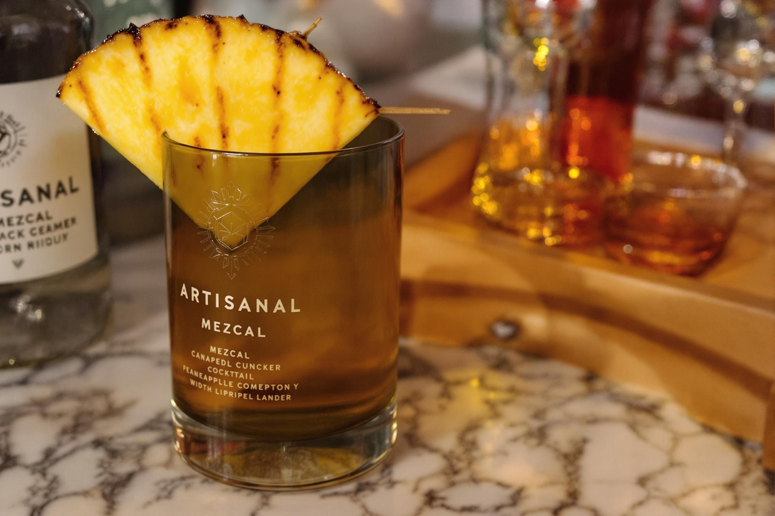 Artisanal mezcal cocktail in a smoked glass, garnished with a caramelized grilled pineapple wedge. The drink's smoky essence mingles with tropical sweetness, creating a visually striking and flavor-rich libation perfect for upscale bars or home mixology enthusiasts.