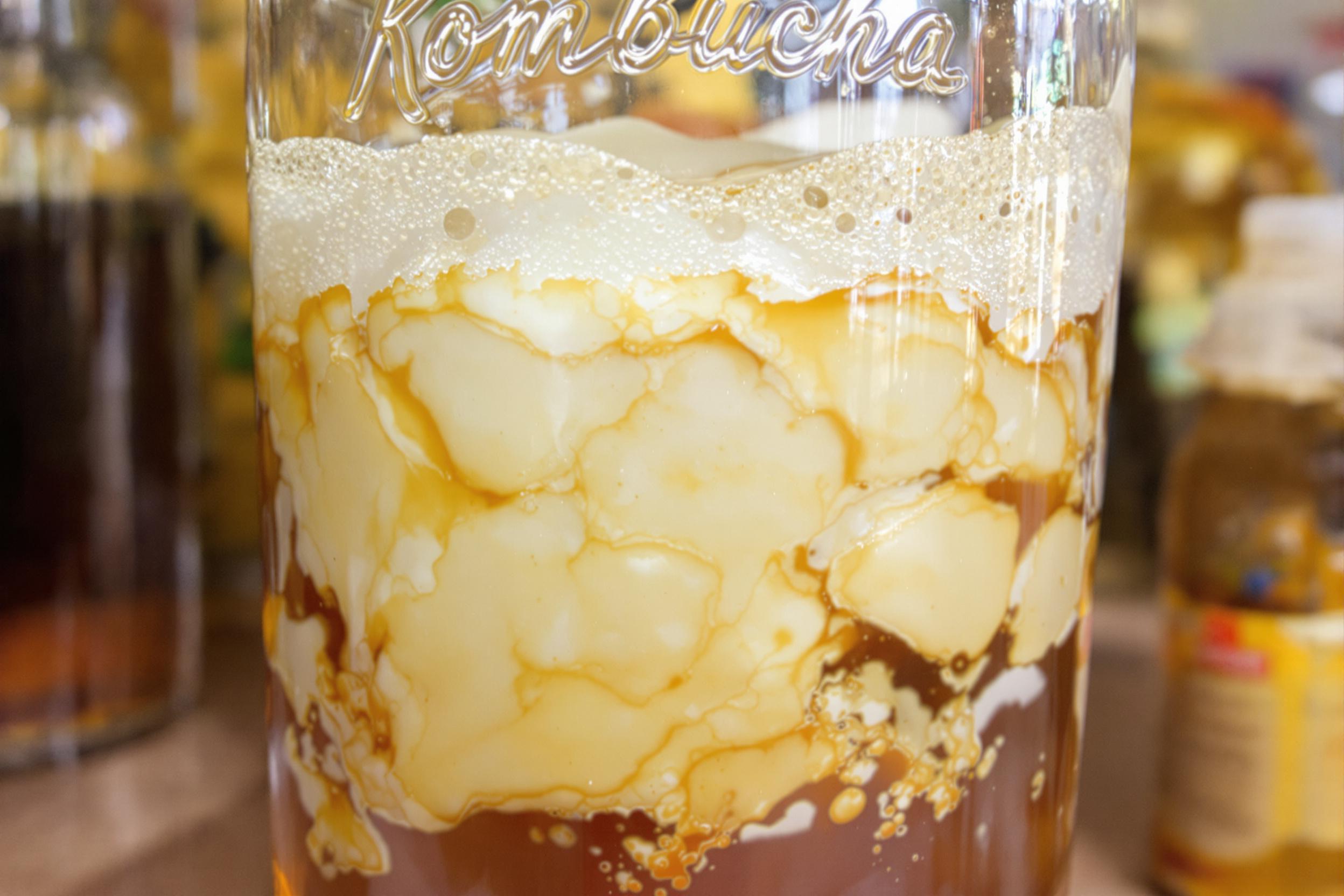 Capture the essence of craft fermentation in this image of kombucha brewing. A large glass jar reveals layers of SCOBY, tea, and bubbles, showcasing the symbiotic culture and fermentation process of this probiotic-rich beverage.