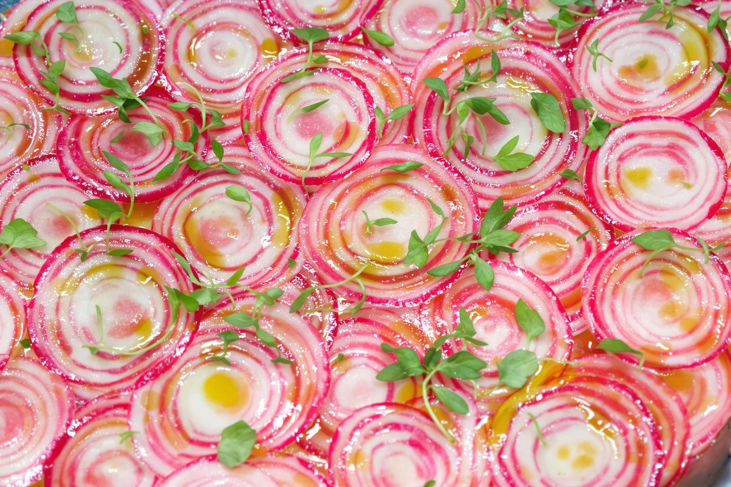 Discover the artistry of vegetable preparation with this stunning watermelon radish carpaccio. Translucent pink and white rings create a mesmerizing pattern, garnished with microgreens and a drizzle of olive oil. A feast for the eyes and palate.