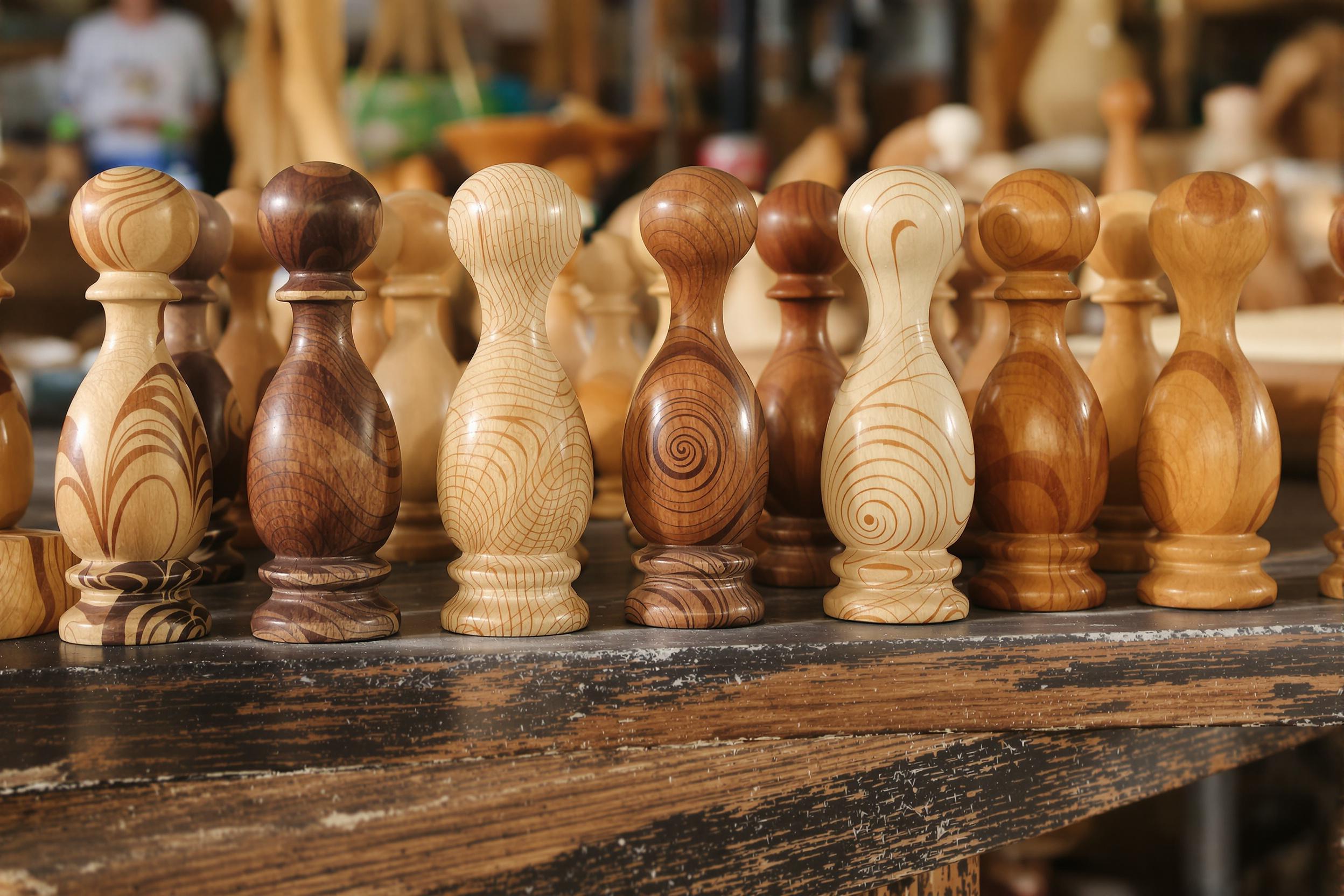 A close-up composition captures an array of intricately handcrafted wooden toys lined on a worn workbench. Each toy showcases fine details, from smooth curves to engraved patterns, reflecting skilled craftsmanship. Natural light softly illuminates their varied grains and warm hues ranging from deep browns to honey tones, inviting exploration into artisanal artistry.