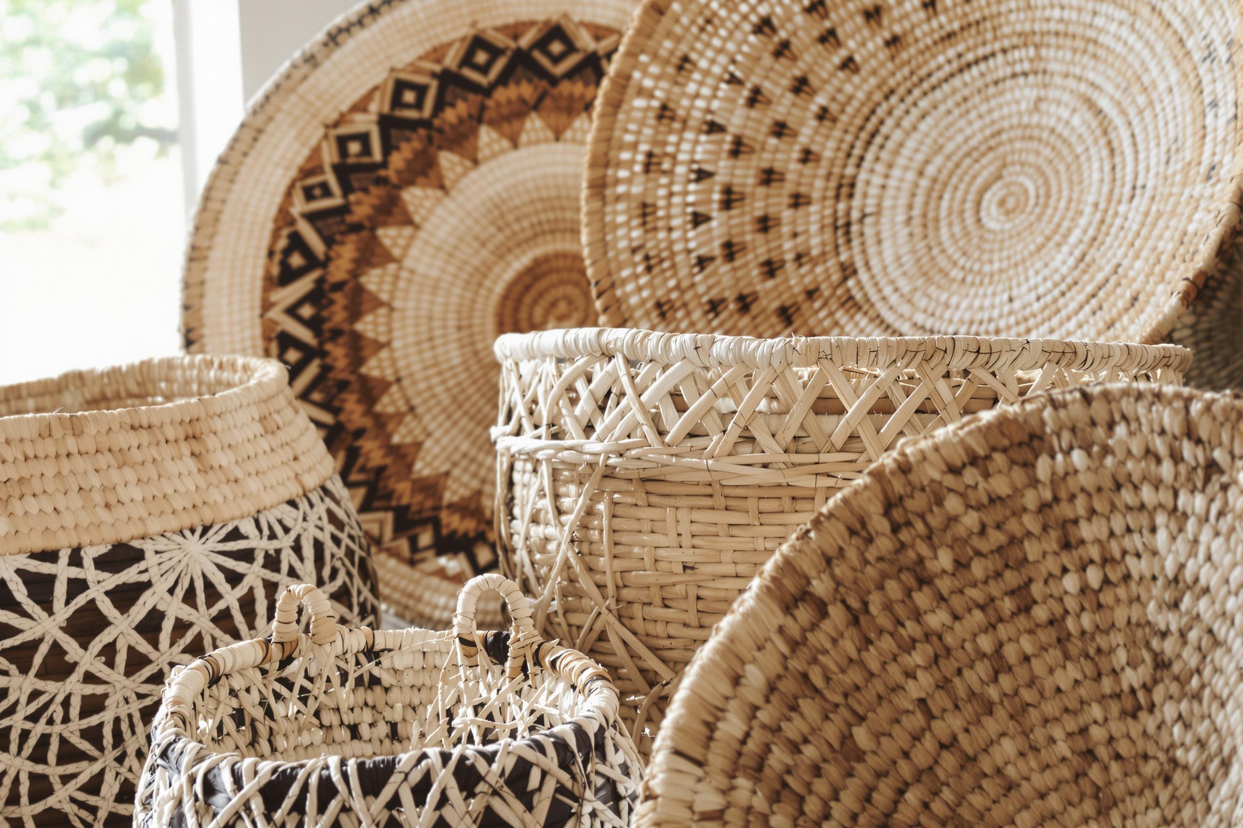 Intricately patterned handwoven baskets are arranged beautifully in a close-up composition. Each basket showcases unique designs from various craft traditions. Soft, natural light filters from one side, enhancing the fine textural weave and the muted palette of earth tones.