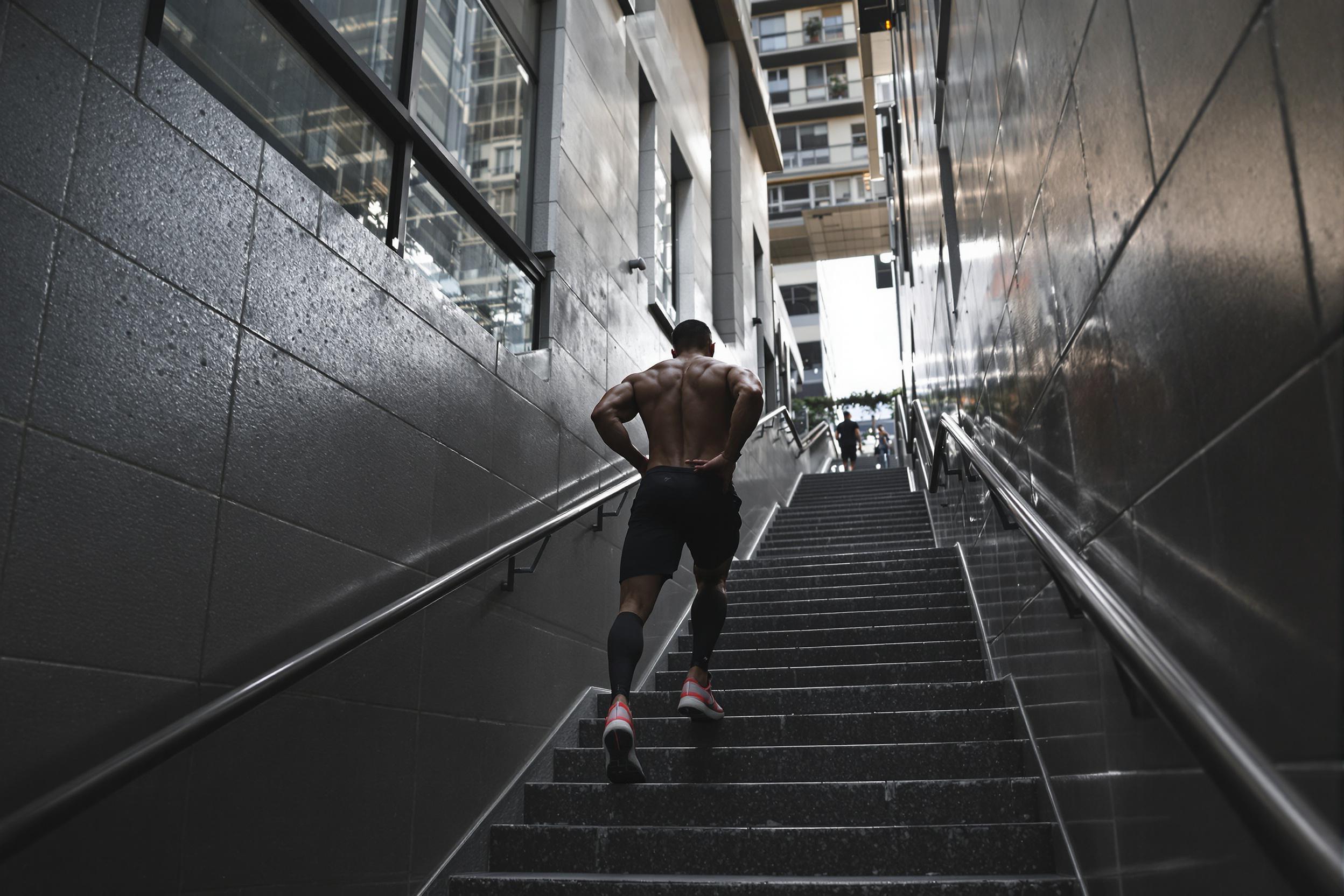 Determined athlete mid-workout on city stairs. Muscular physique silhouetted against modern architecture. Dynamic composition capturing strength, endurance, and urban health consciousness.