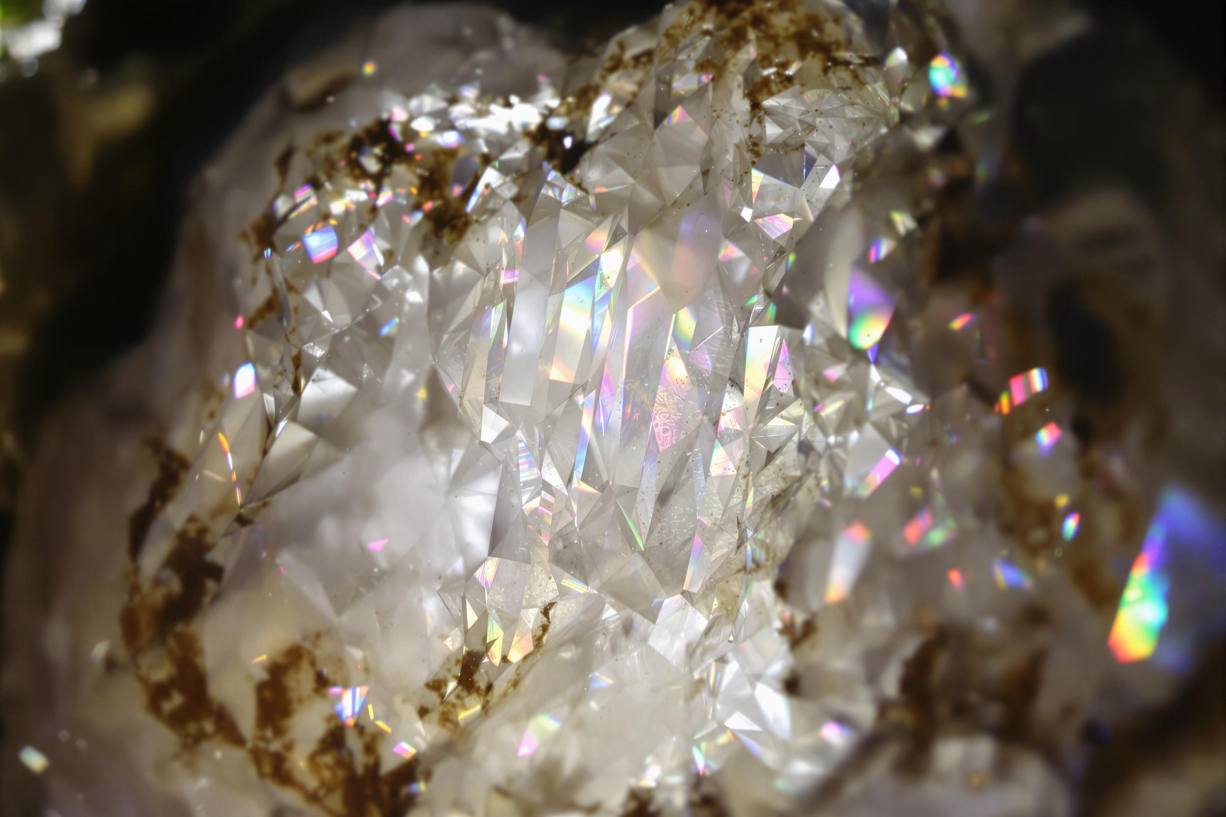 A macro shot captures the depths of a quartz crystal geode illuminated by soft, natural window light. Intricate facets glimmer with rainbow reflections, contrasting against the rough outer stone matrix. Fine details reveal subtle etchings and inclusions, emphasizing the raw beauty of this natural formation.