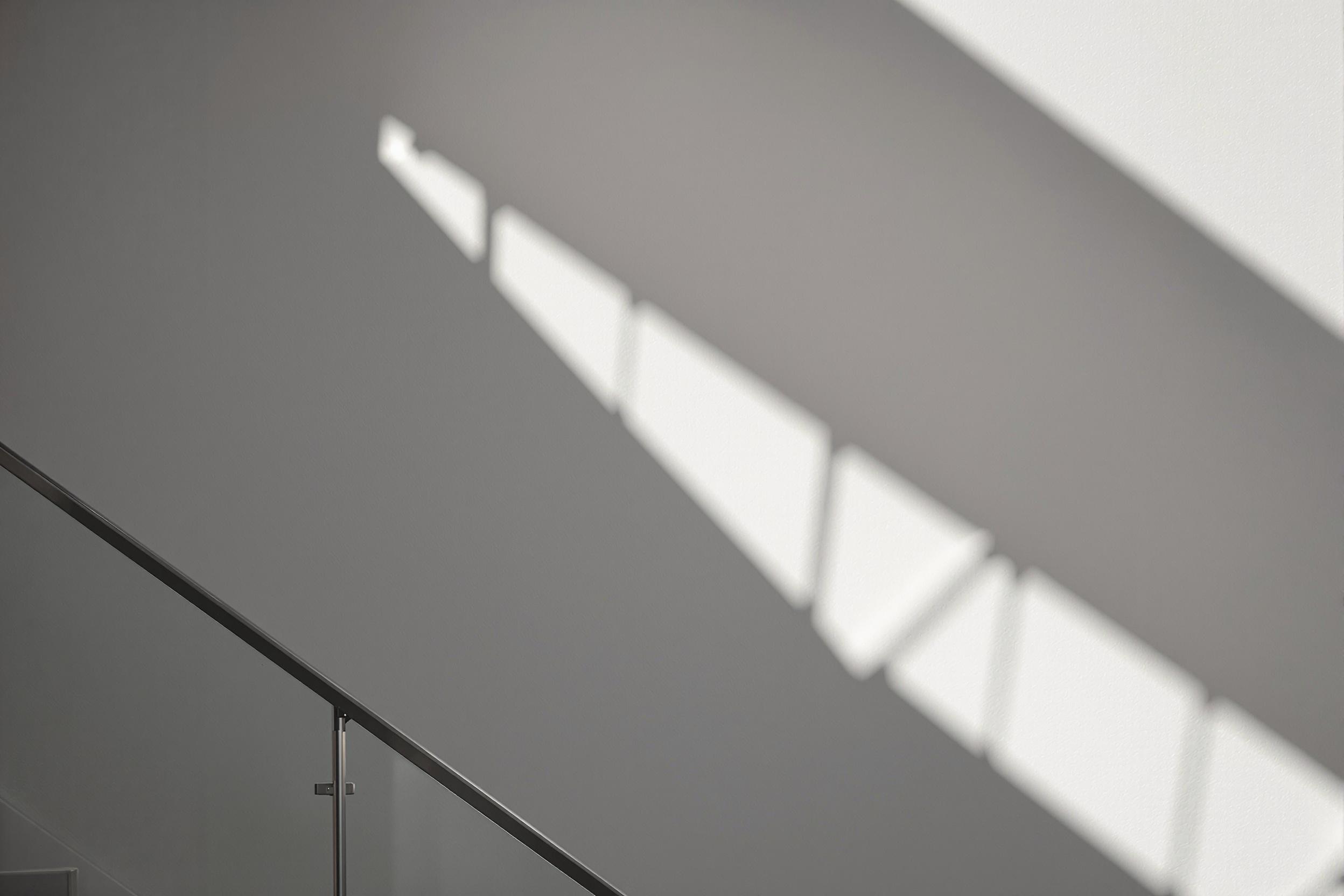 A striking minimalist photograph of a modern staircase, showcasing clean lines and geometric shadows. The composition emphasizes the interplay between light and architecture, creating a visually compelling abstract image.