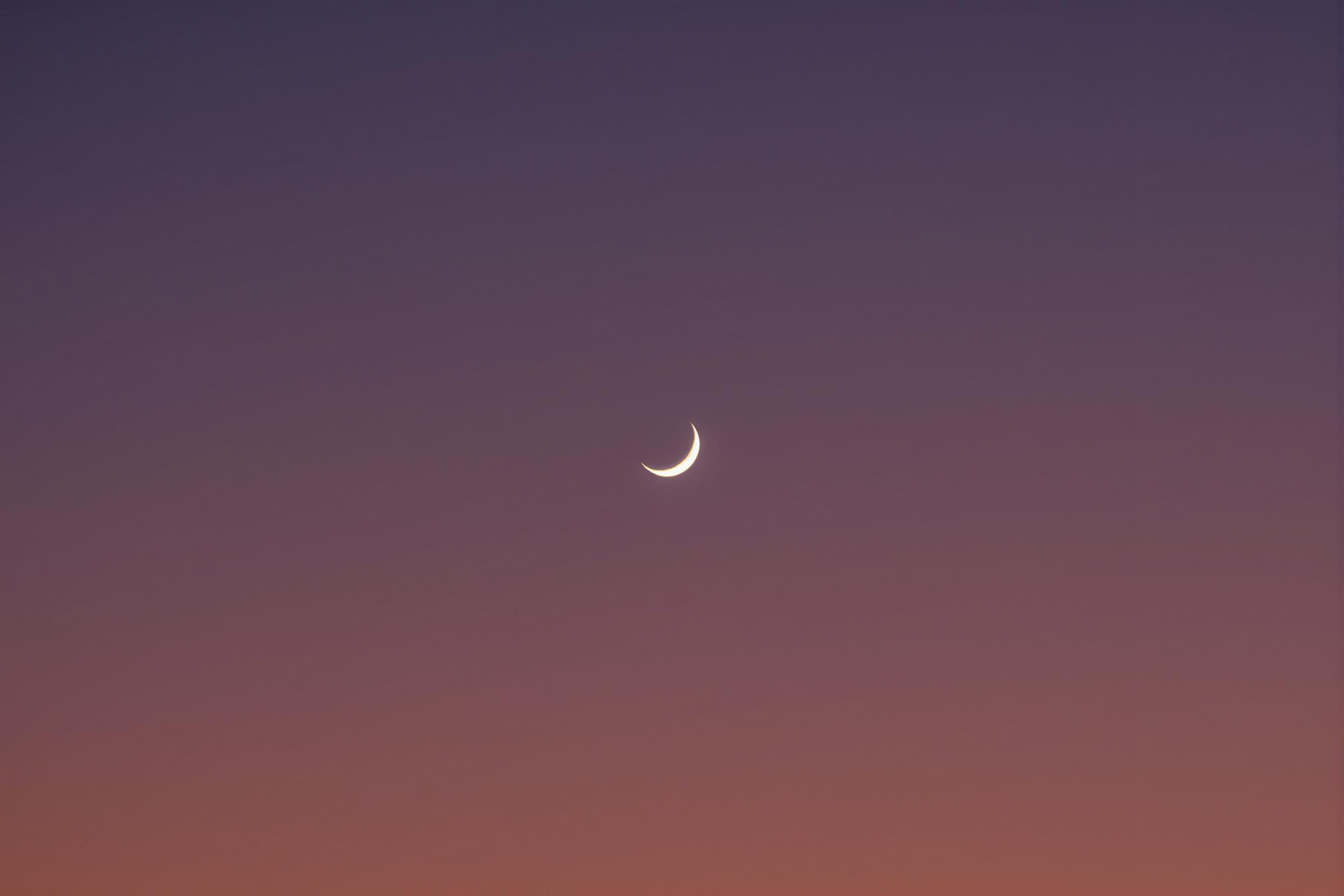 A captivating minimalist photograph capturing the essence of a lunar eclipse. A slender crescent moon silhouette stands out against a gradient twilight sky, creating a striking contrast between light and shadow.