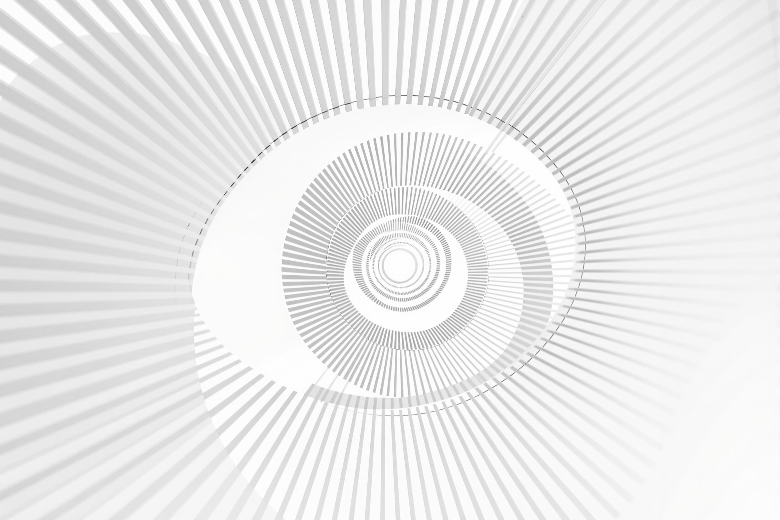 A striking minimalist composition featuring a pristine white spiral staircase. The curved lines create a mesmerizing geometric pattern against a stark white background, emphasizing negative space and architectural simplicity.