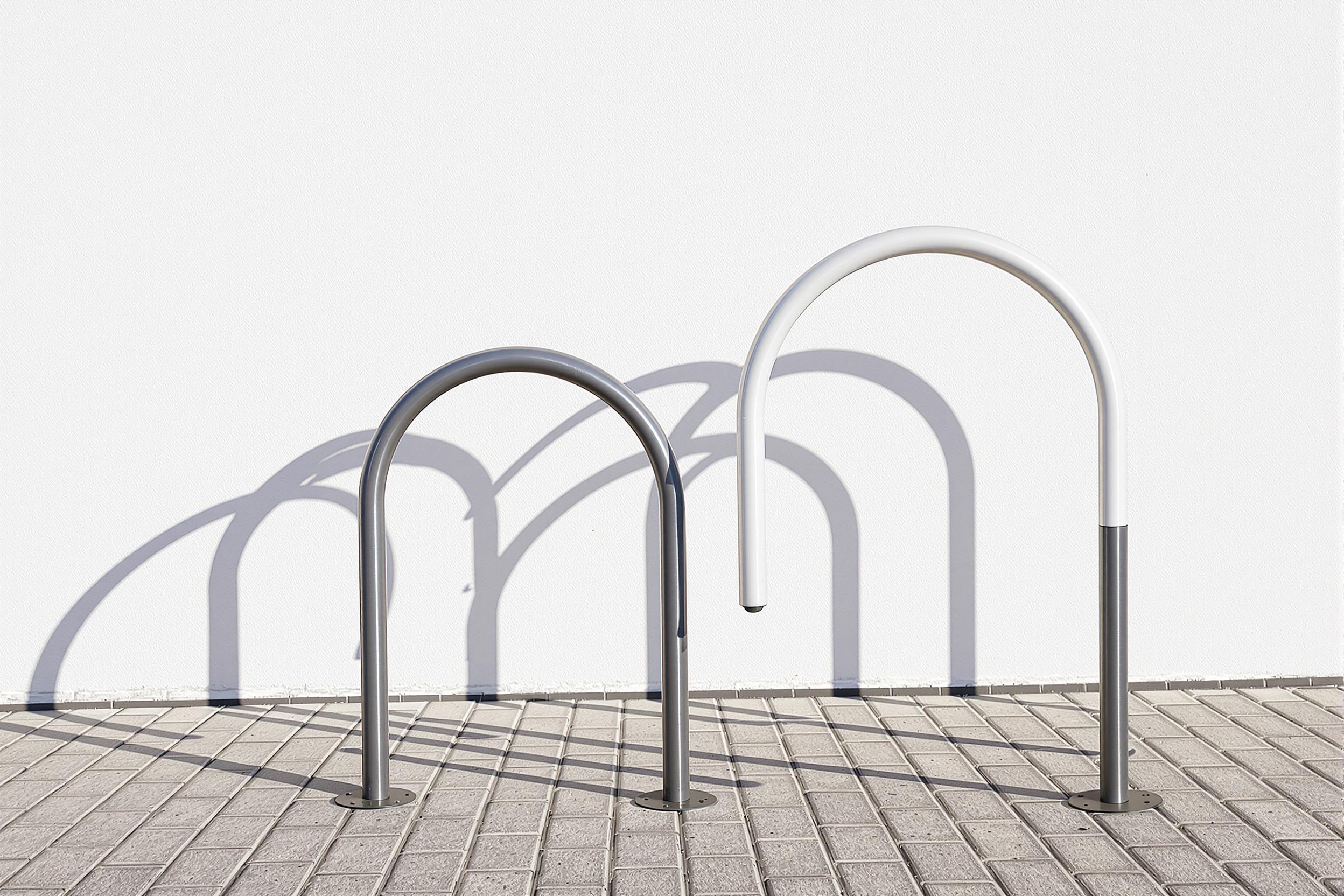 A sleek, curved bicycle rack stands empty against a stark white wall, casting intricate shadows. The interplay of light and metal creates a captivating study in urban minimalism and functional design.