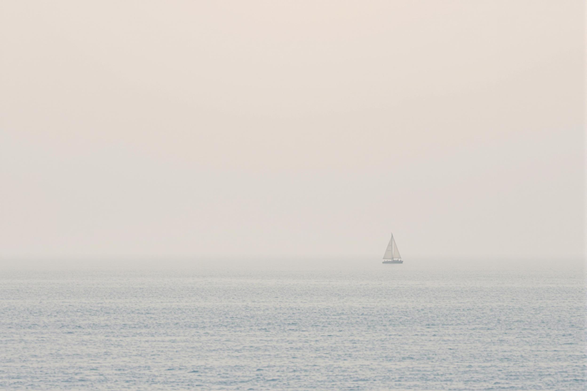 A lone sailboat silhouette against a misty horizon, embodying serenity and adventure. Soft, muted colors blend sea and sky, creating a dreamy minimalist seascape that evokes wanderlust and tranquility.