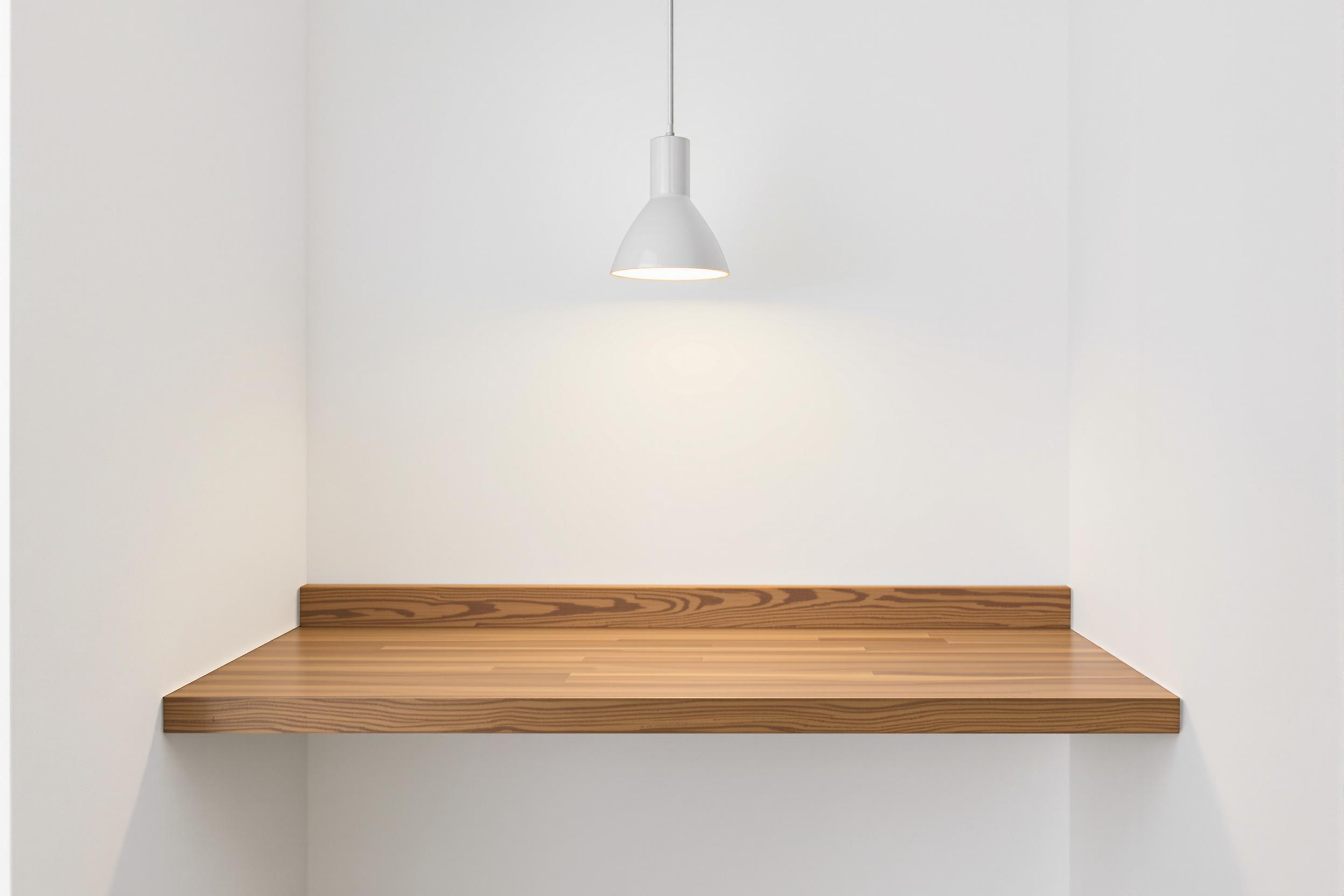 A minimalist home office corner featuring a floating wooden shelf against a white wall, serving as a compact desk. A single, sleek pendant light hangs above, casting a warm glow. The composition emphasizes clean lines, functionality, and serene simplicity.