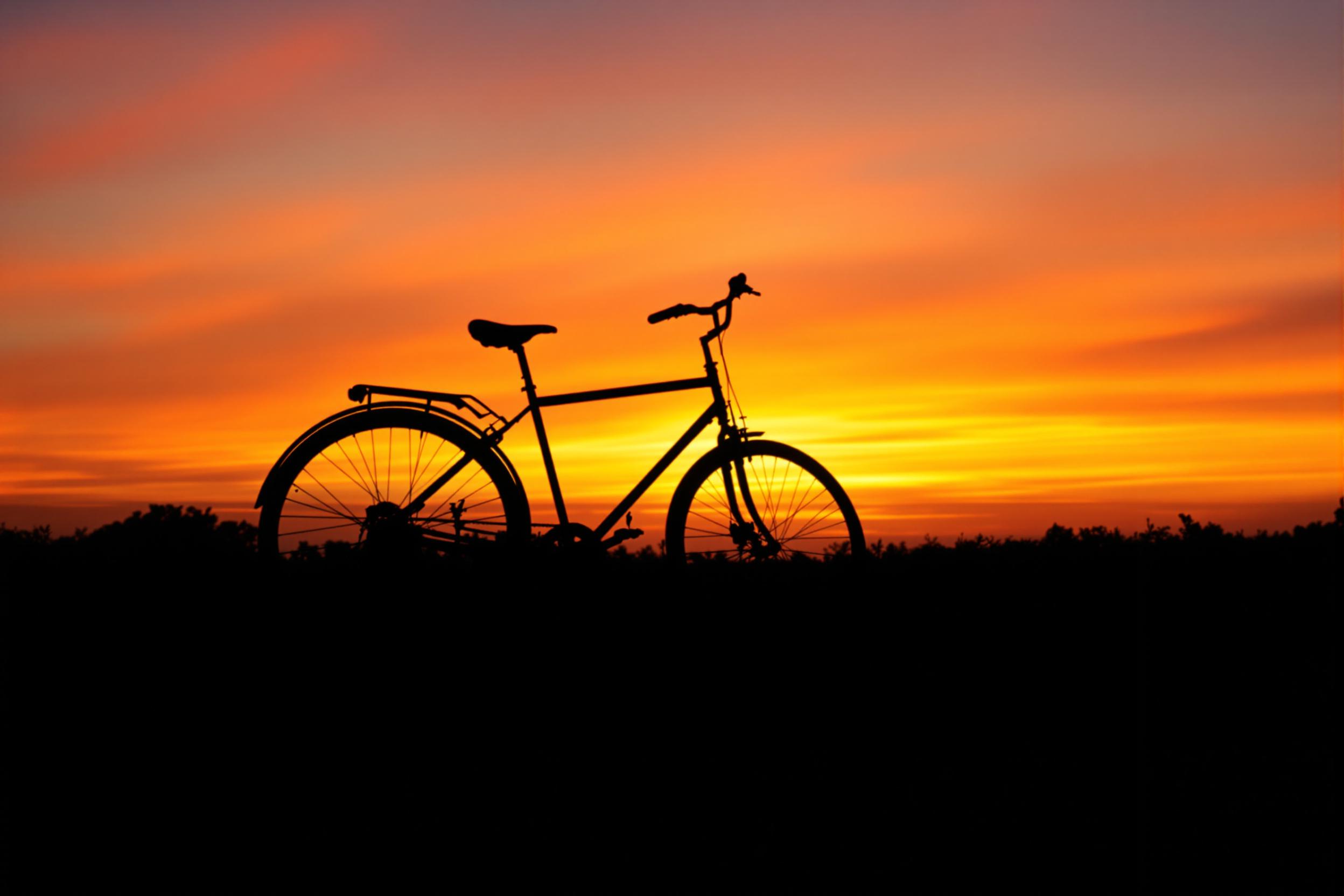 A lone bicycle silhouette stands out against a vibrant sunset sky, creating a striking minimalist composition. The image captures the essence of urban mobility and environmental consciousness, with warm hues painting the horizon.