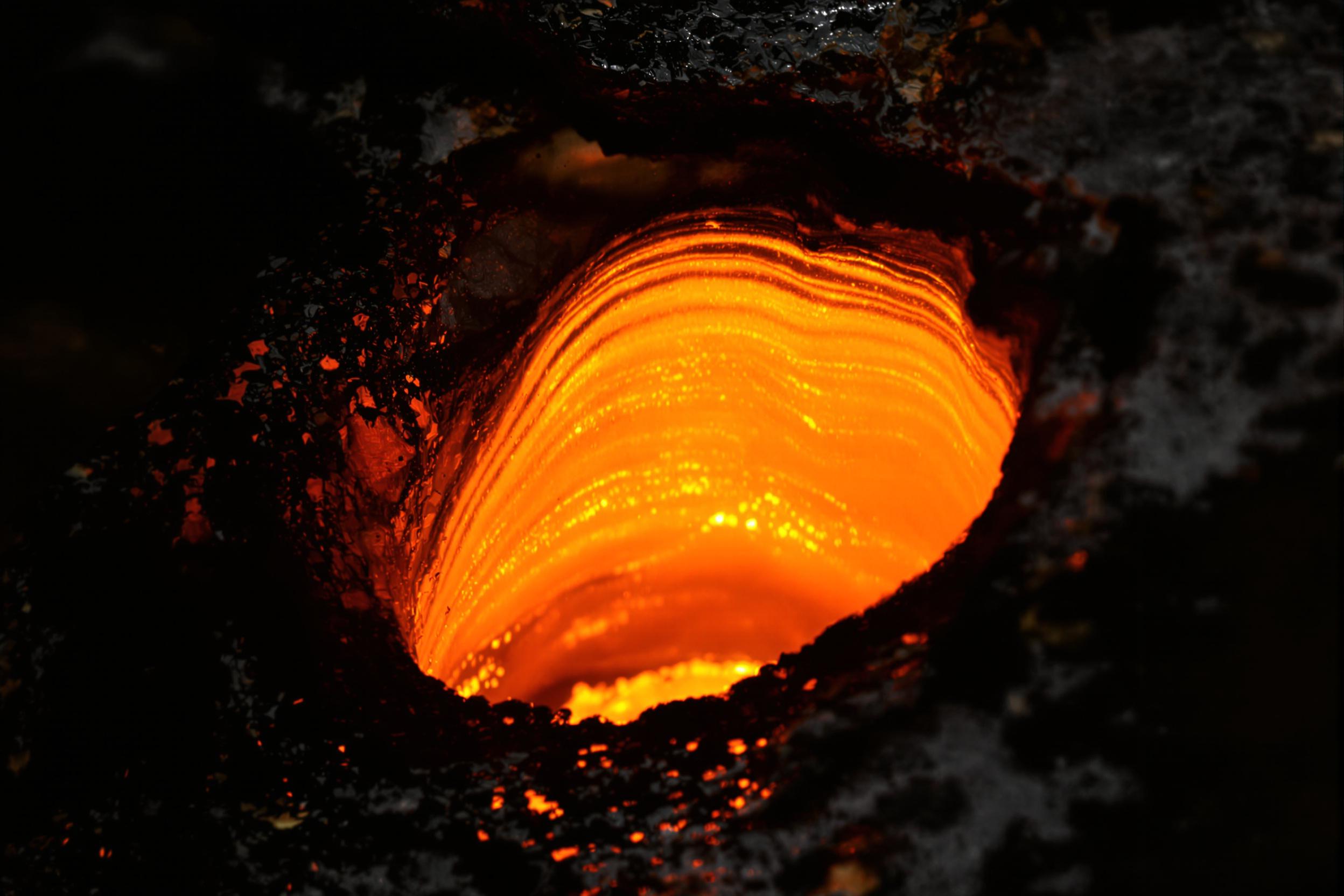 The glowing semi-liquid form of molten glass is captured in exquisite close-up, its fiery orange depths radiating heat. Tiny ridges ripple across the curved surface as raw edges blend seamlessly into deep shadow. Directional lighting highlights minute imperfections, evoking the intensity of craftsmanship in this ancient artistry.