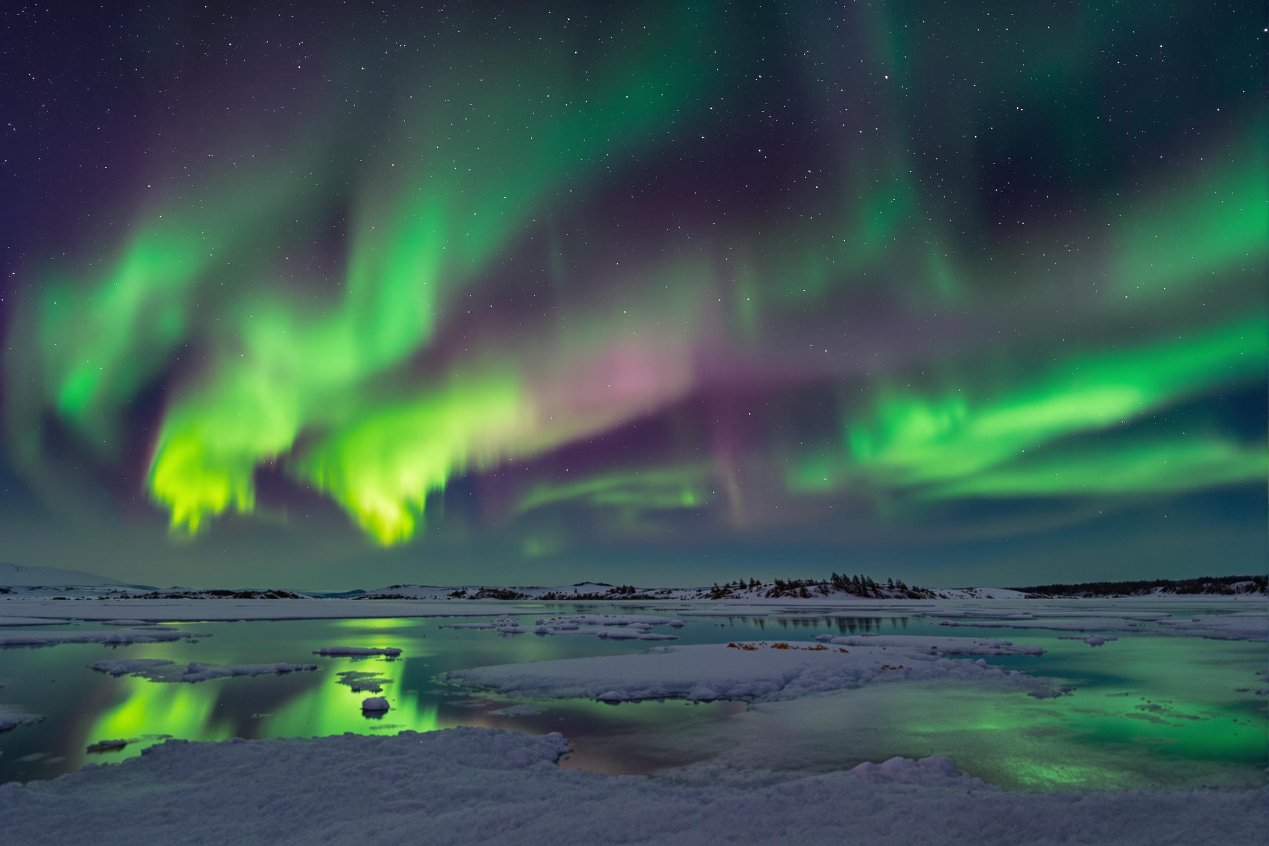 A breathtaking view of the Northern Lights illuminating a snowy landscape. Vibrant greens and purples dance across the night sky, reflecting on the pristine snow below. Perfect for nature lovers.