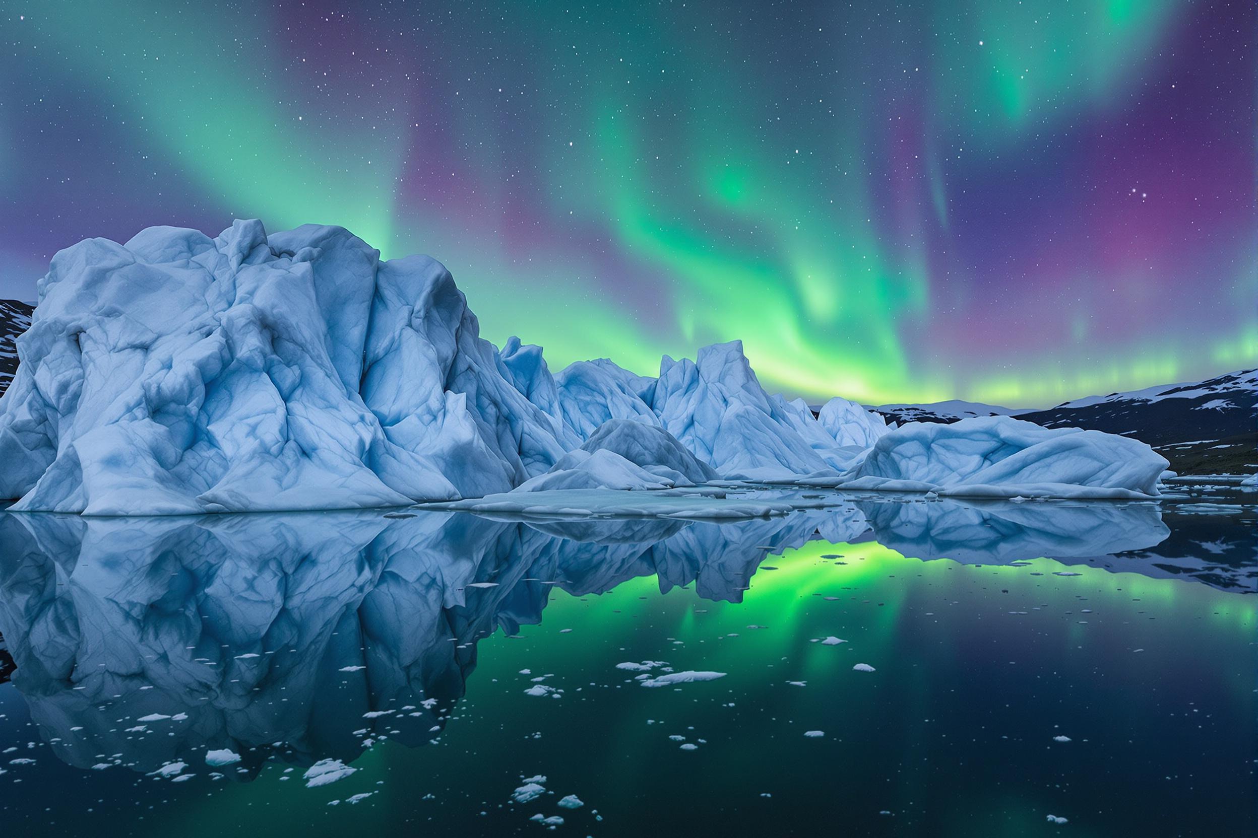 Witness the ethereal beauty of a remote glacial lagoon under the dancing lights of the Aurora Borealis. Massive icebergs float serenely in the mirror-like water, their crystalline surfaces reflecting the vibrant greens and purples of the Northern Lights above. This captivating scene showcases the raw power and delicate balance of nature in the Arctic.