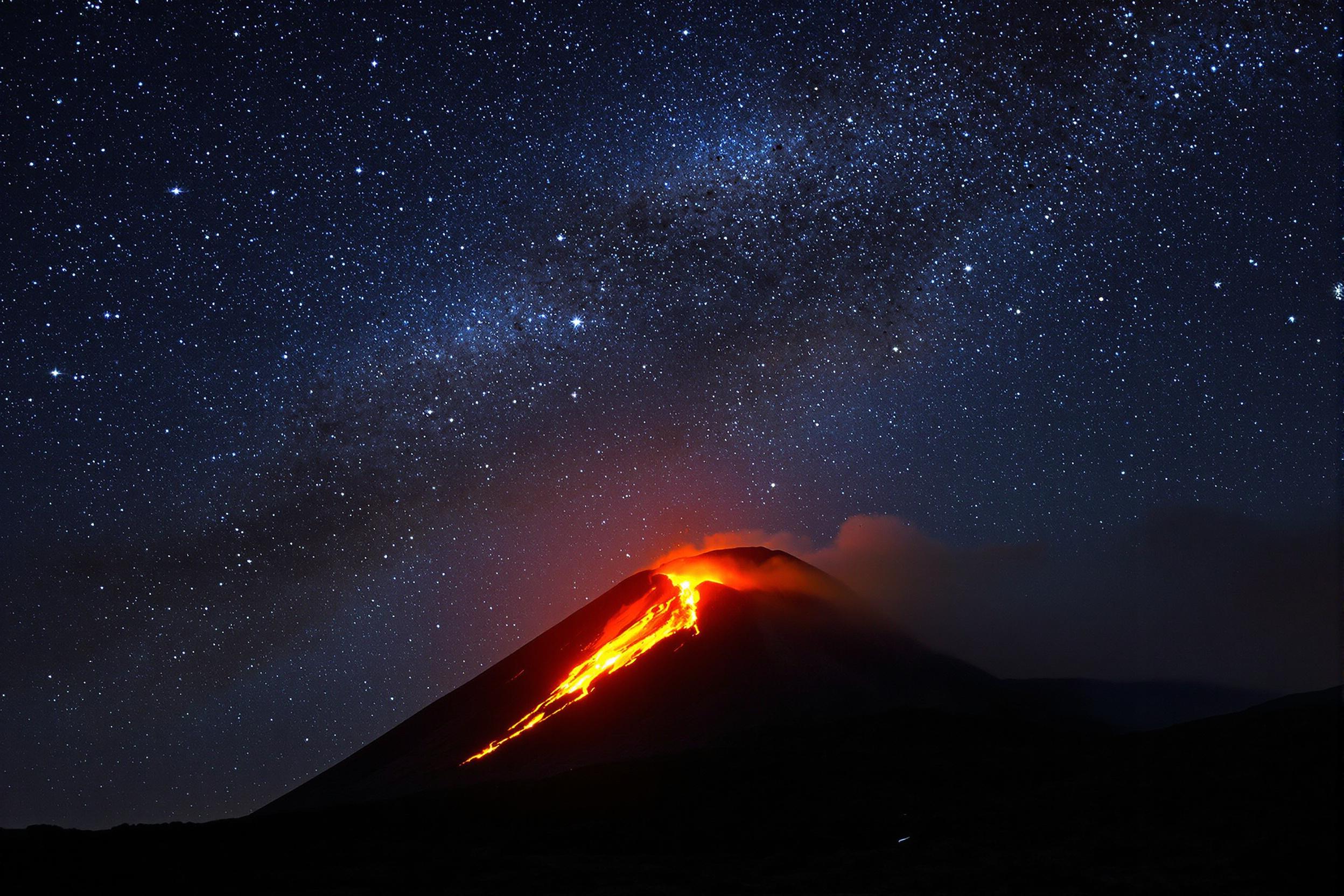 Witness the raw power of nature as an active volcano erupts against a backdrop of a starry night sky. Glowing lava flows down the mountainside, creating a mesmerizing contrast with the twinkling stars above. This awe-inspiring scene captures the dynamic forces shaping our planet.