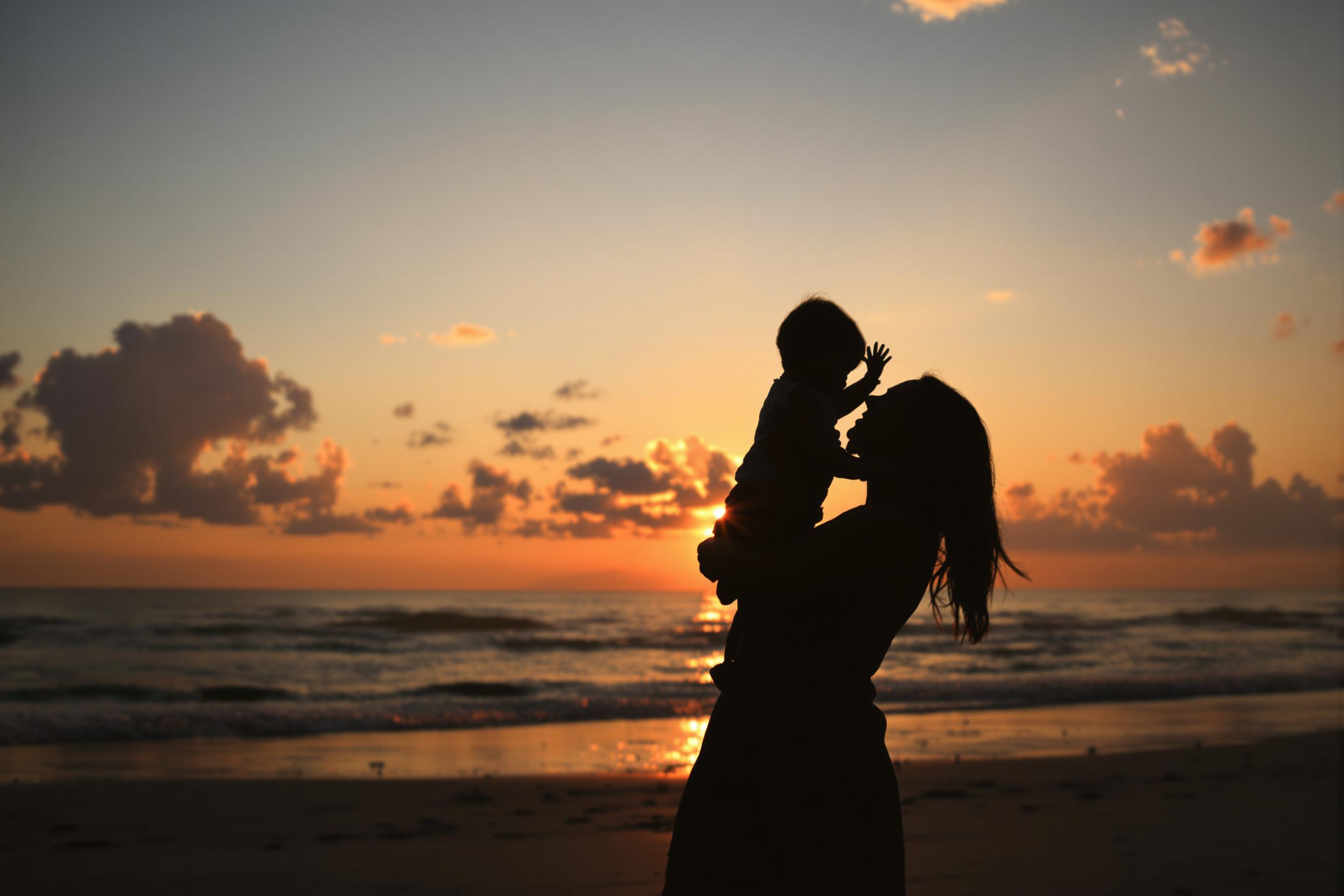 A silhouetted mother and child embracing on a beach at sunset. This emotive image conveys love, family bonds, and the beauty of parenthood, perfect for emotional and lifestyle themes.