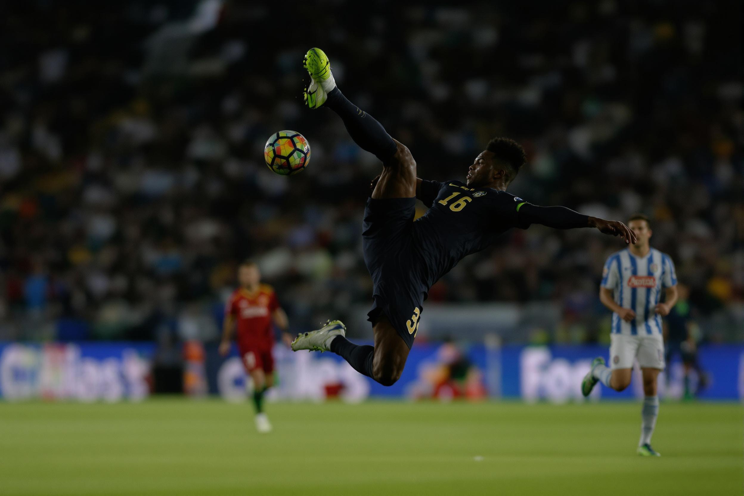 Capture the intensity of a soccer match with this dynamic image of a player executing a mid-air bicycle kick. The athlete's muscular form is silhouetted against a blurred stadium background, showcasing power and agility in action.