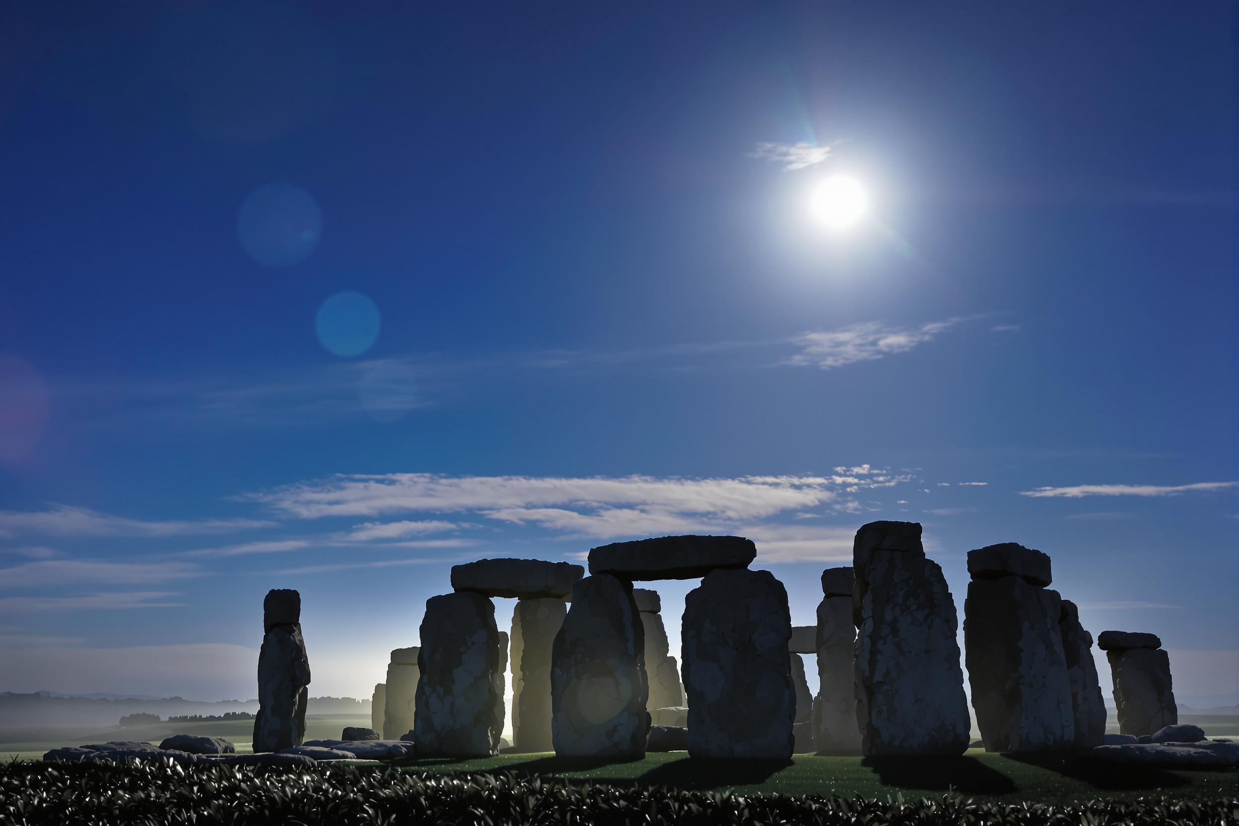 Under a clear moonlit sky, the iconic structures of Stonehenge stand silhouetted against the celestial expanse. Cool blue hues dominate as silvery moonlight illuminates the rugged stone texture, creating intricate shadows. Surrounding fields are cloaked in faint mist, enhancing mystique in this timeless prehistoric site.