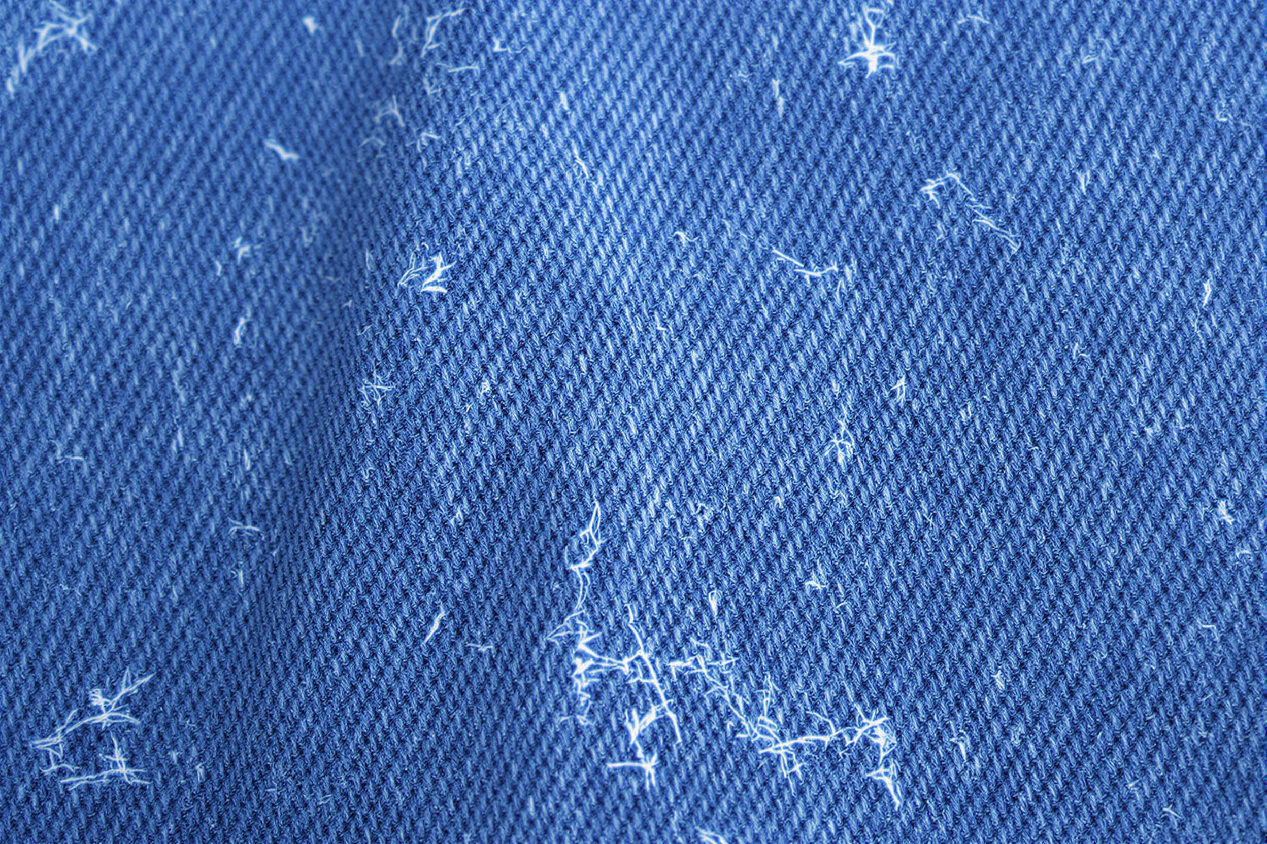 Extreme close-up of well-worn denim fabric, showcasing intricate weave patterns and faded indigo hues. The photograph captures the rugged texture, frayed edges, and subtle variations in color, highlighting the beauty in everyday wear and tear.