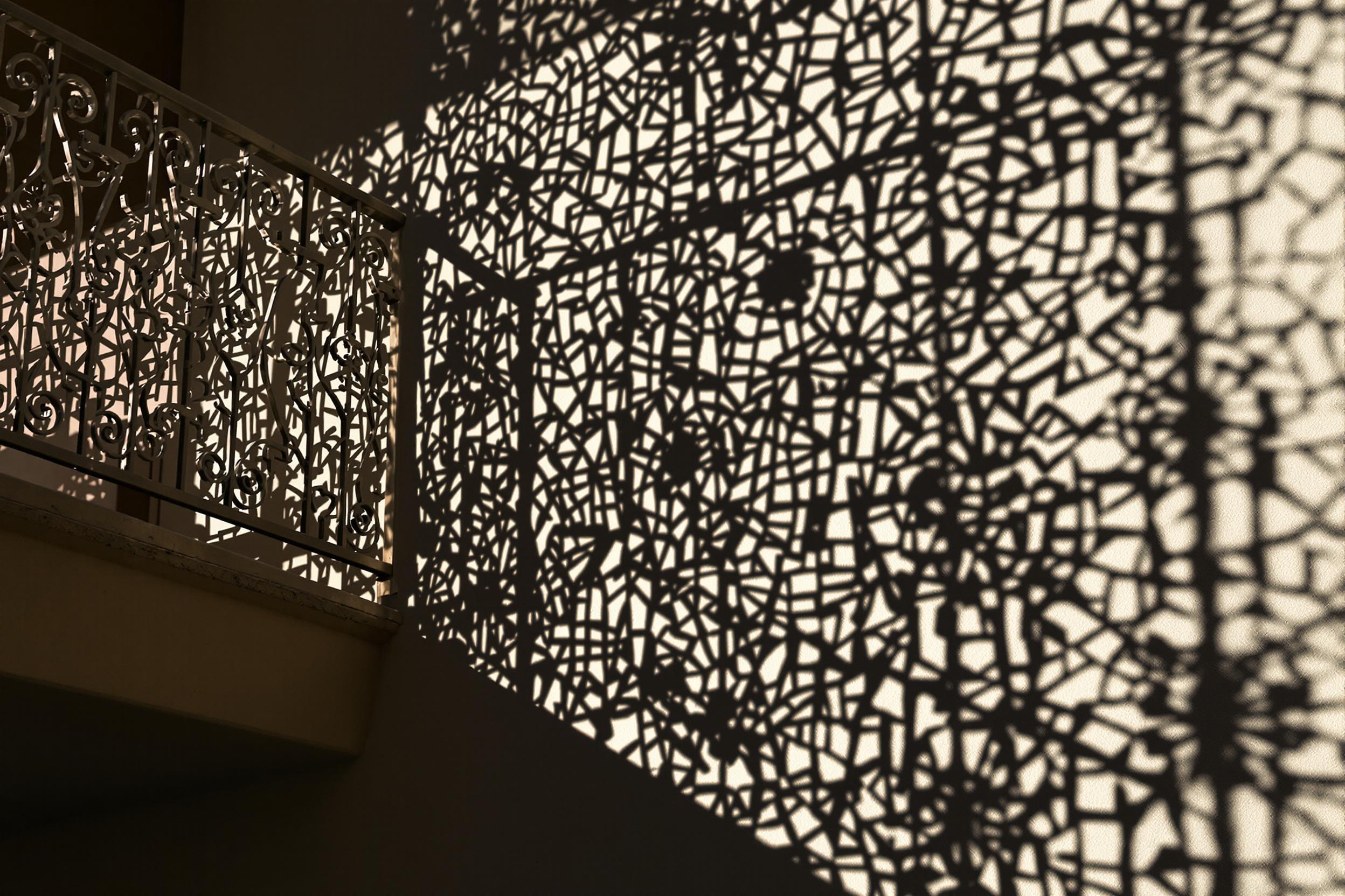 Mesmerizing geometric patterns created by wrought iron balcony railings cast intricate shadows on a sun-drenched wall. The interplay of light and shadow forms a captivating tessellation, showcasing urban architecture's hidden artistry.