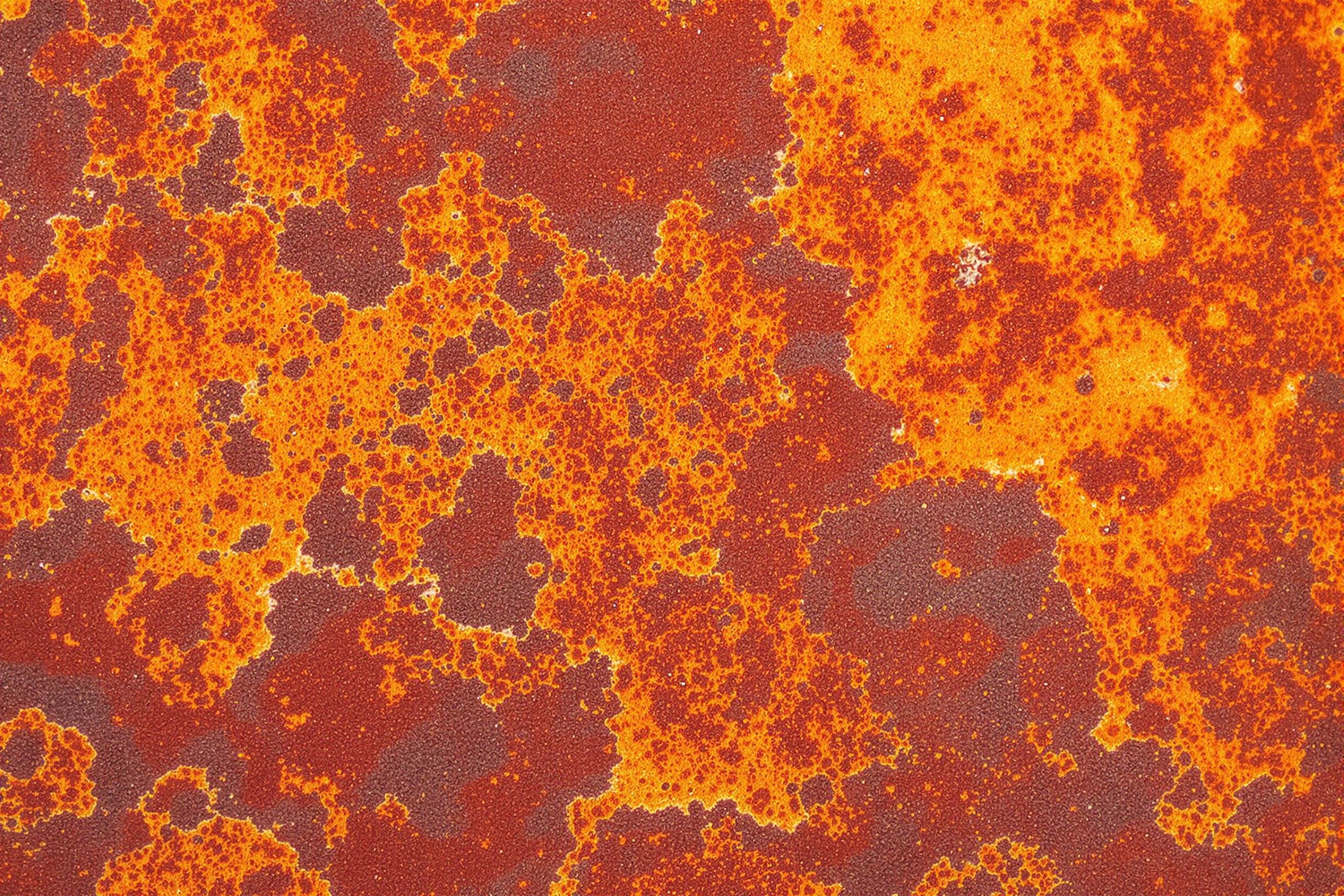 Close-up of a weathered metal surface showcasing intricate rust patterns in vibrant oranges, reds, and browns. The abstract composition reveals nature's artistry in decay, perfect for industrial design or vintage aesthetics.