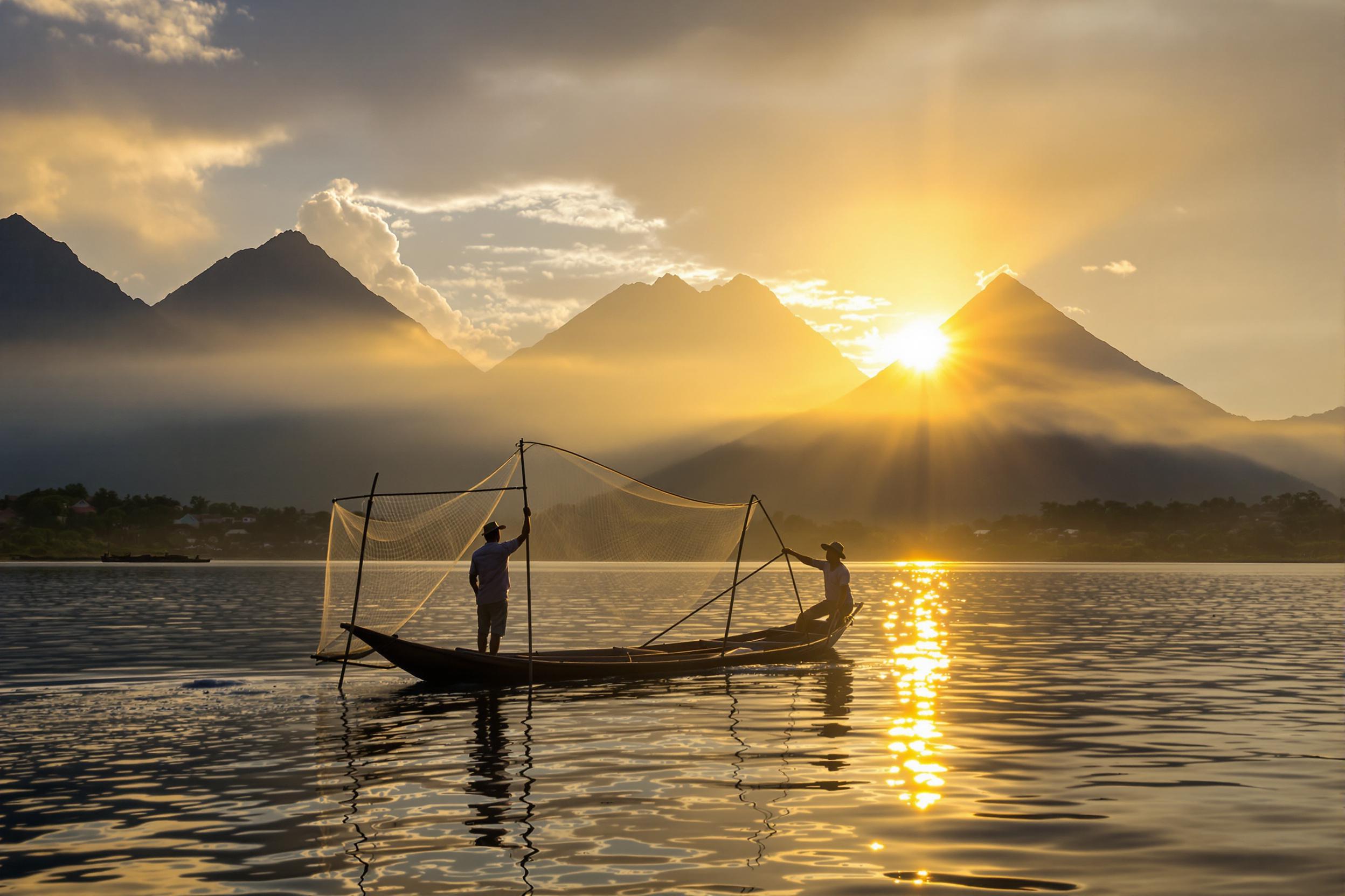 Experience the serene awakening of Lake Atitlán, Guatemala. A traditional Mayan fisherman casts his net from a wooden cayuco boat, silhouetted against the backdrop of three majestic volcanoes. The golden light of dawn reflects off the calm waters, illuminating the misty shoreline dotted with colorful villages.