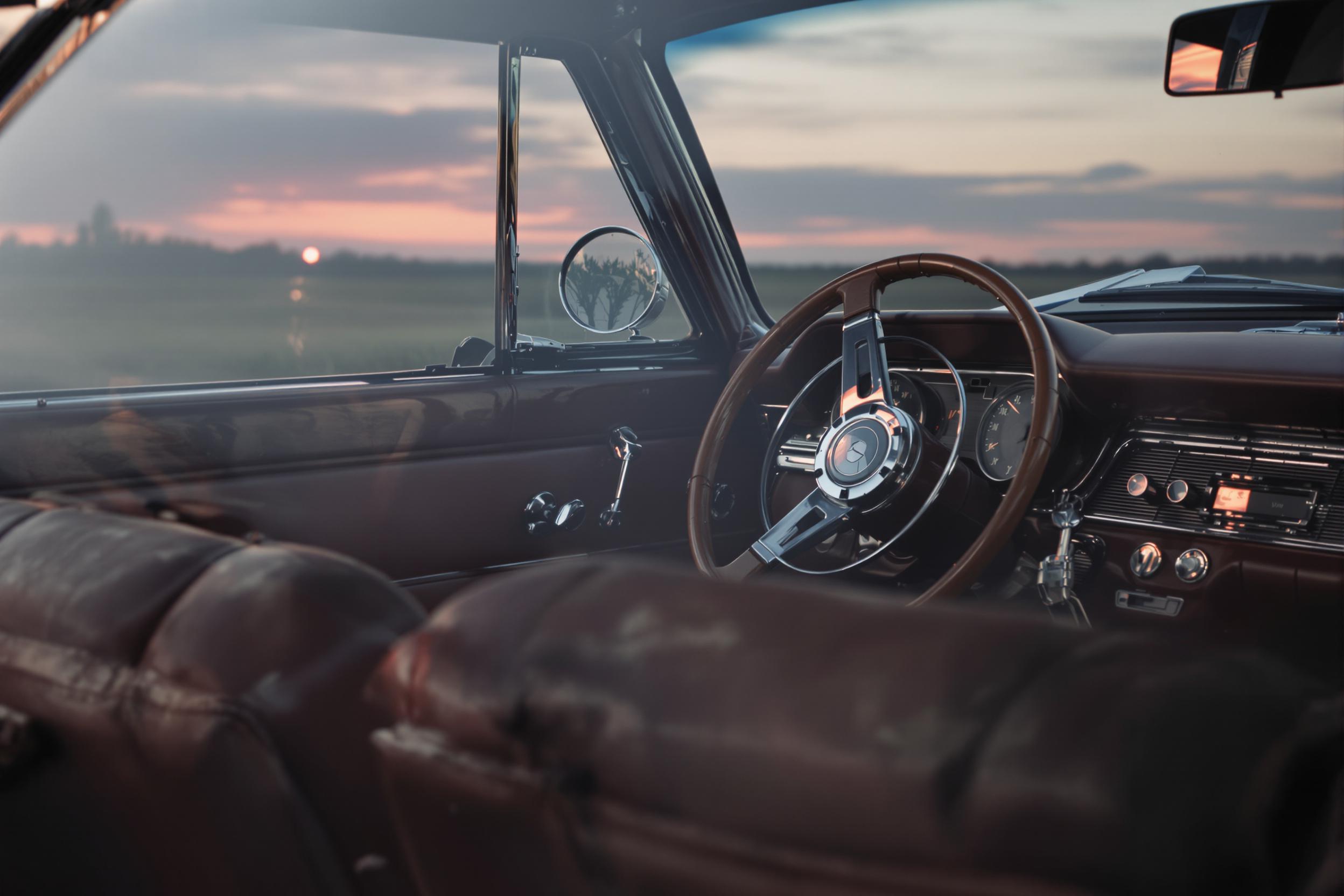 A cinematic angle captures the detailed interior of a classic vintage car during twilight. Deep brown leather seats show subtle wear, while chrome accents gleam under soft, ambient light. The steering wheel's wooden rim reflects faint hues of an orange-pink sunset peeking through the windshield, blending nostalgia and elegance.