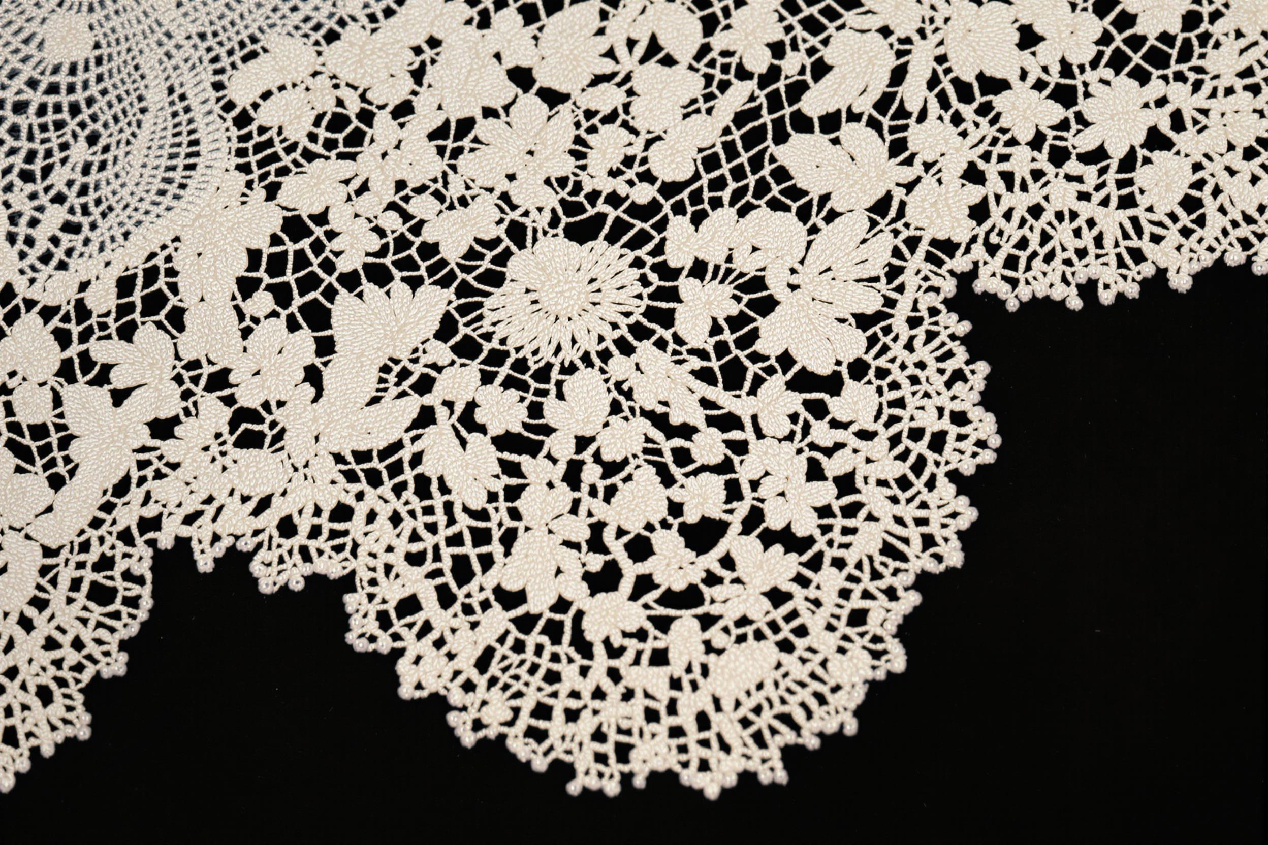 An extreme close-up reveals exquisite lacework adorning a vintage dress, showcasing intricate patterns of floral motifs interspersed with delicate scallops. The fine threads create a mesmerizing tapestry of textures, their cream hue contrasting beautifully against the dark backdrop. Subtle shadows add depth, enhancing the craftsmanship's beauty and inviting admiration for this timeless art form.