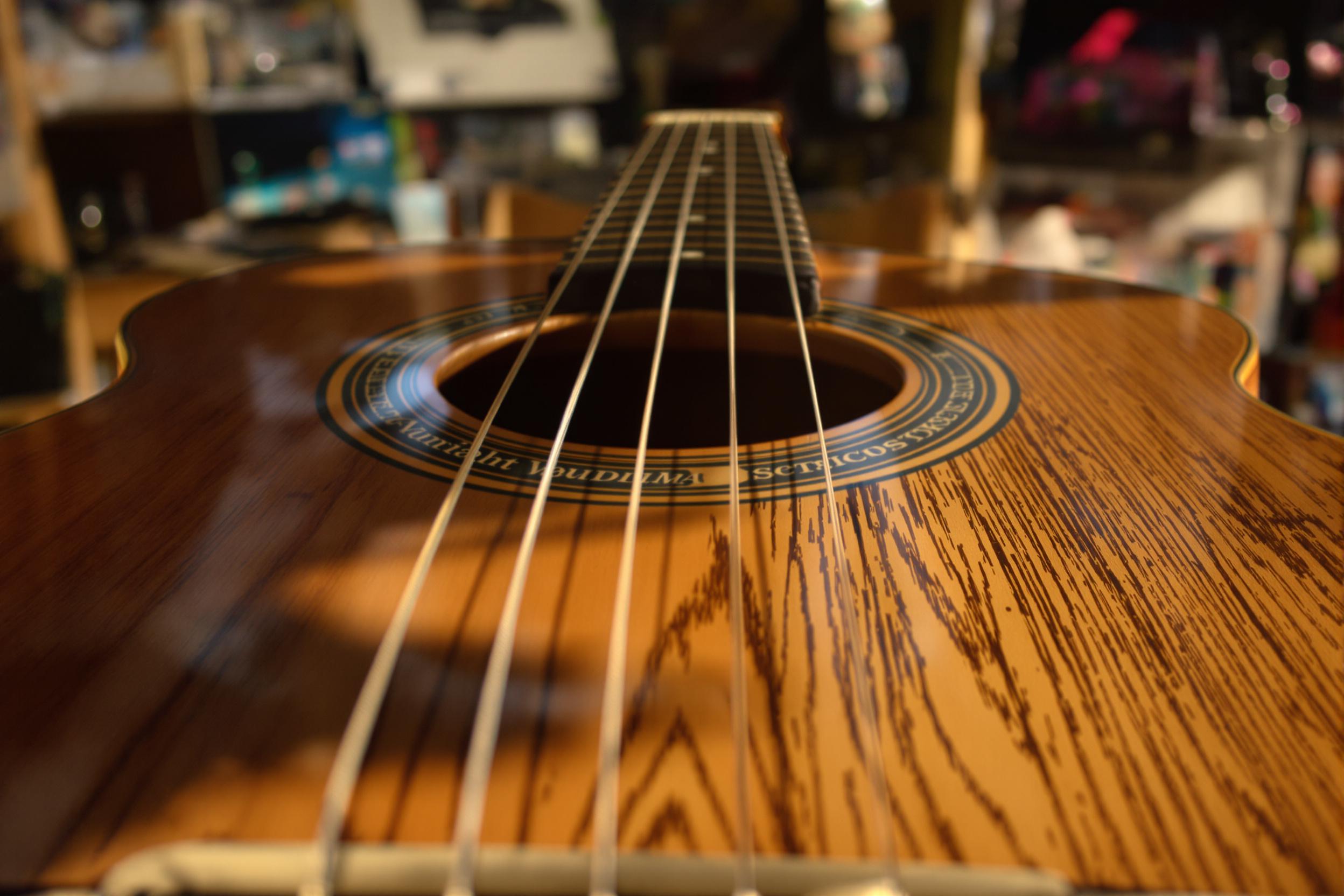 A close-up showcases a vintage guitar elegantly resting on a rustic wooden chair. The warm late afternoon light bathes the polished wooden surface, highlighting its rich grain and subtle imperfections. Each string gleams softly, while the blurred backdrop hints at a cozy room filled with cherished music memorabilia, enhancing the character of this timeless instrument.