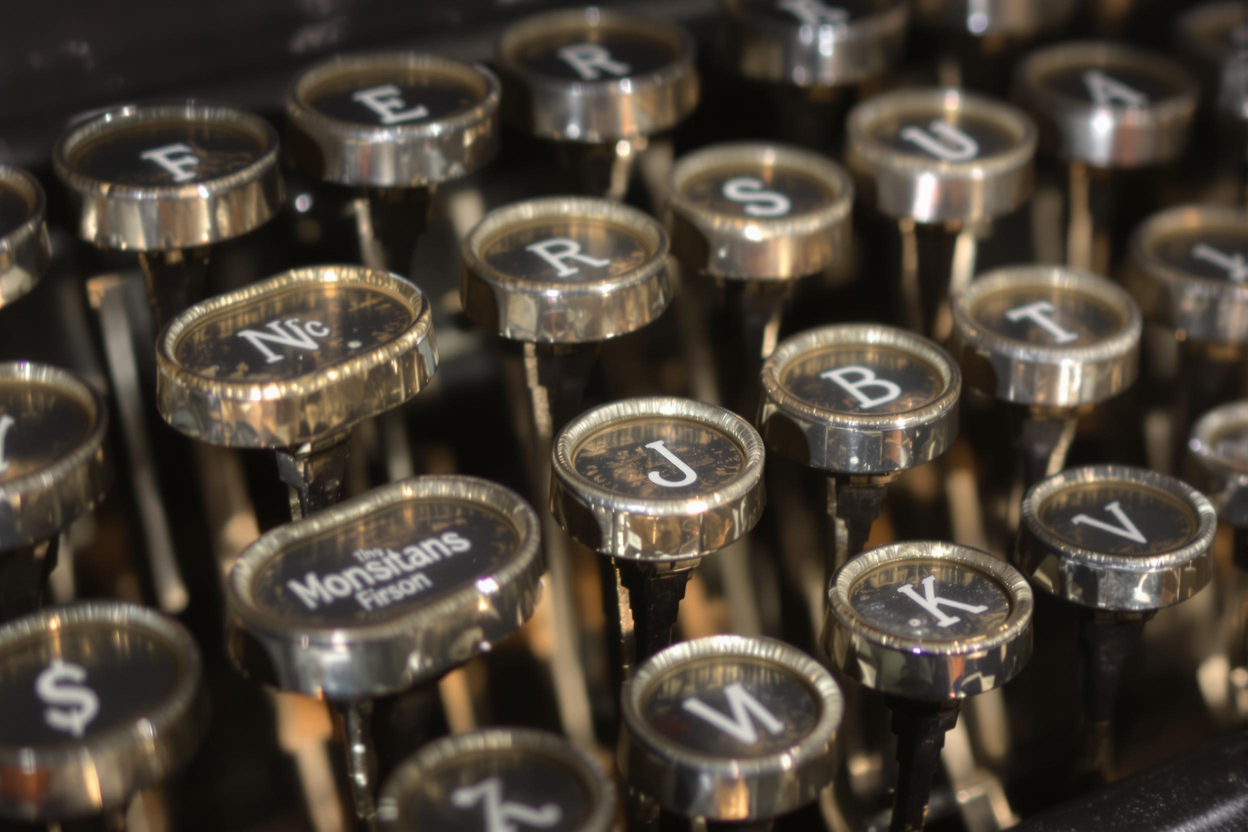 A close-up shot features an array of vintage typewriter keys, their glossy surfaces reflecting warm natural light. Each key showcases elegant lettering, aged patinas, and varying textures that tell stories of times gone by. Subtle shadows create depth, while the surrounding blurred background draws attention to the intricate designs and craftsmanship of the typewriter.