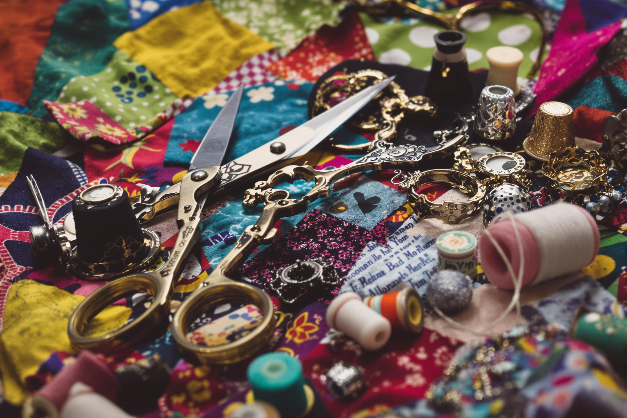 An intimate close-up reveals vintage sewing tools meticulously arranged atop a vibrant patchwork of fabrics. Scissors gleam in the midday light, alongside intricate thimbles and spools of colorful threads. The textured textiles create a dynamic background, showcasing a tapestry of patterns and hues—each tool reflecting craft and history.