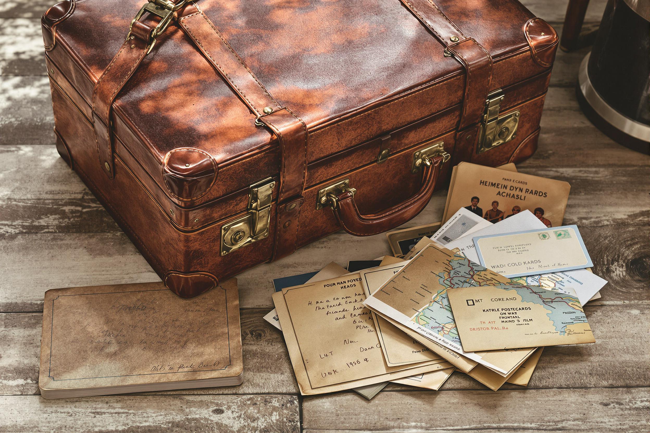 A vintage leather suitcase rests on a weathered wooden floor, exuding nostalgia. Its worn surface displays intricate creases and metal clasps, hinting at many adventures. Surrounding it are open travel memorabilia, including aged postcards and a folded map. Soft, natural light bathes the scene, highlighting the rich textures and inviting exploration of past journeys.