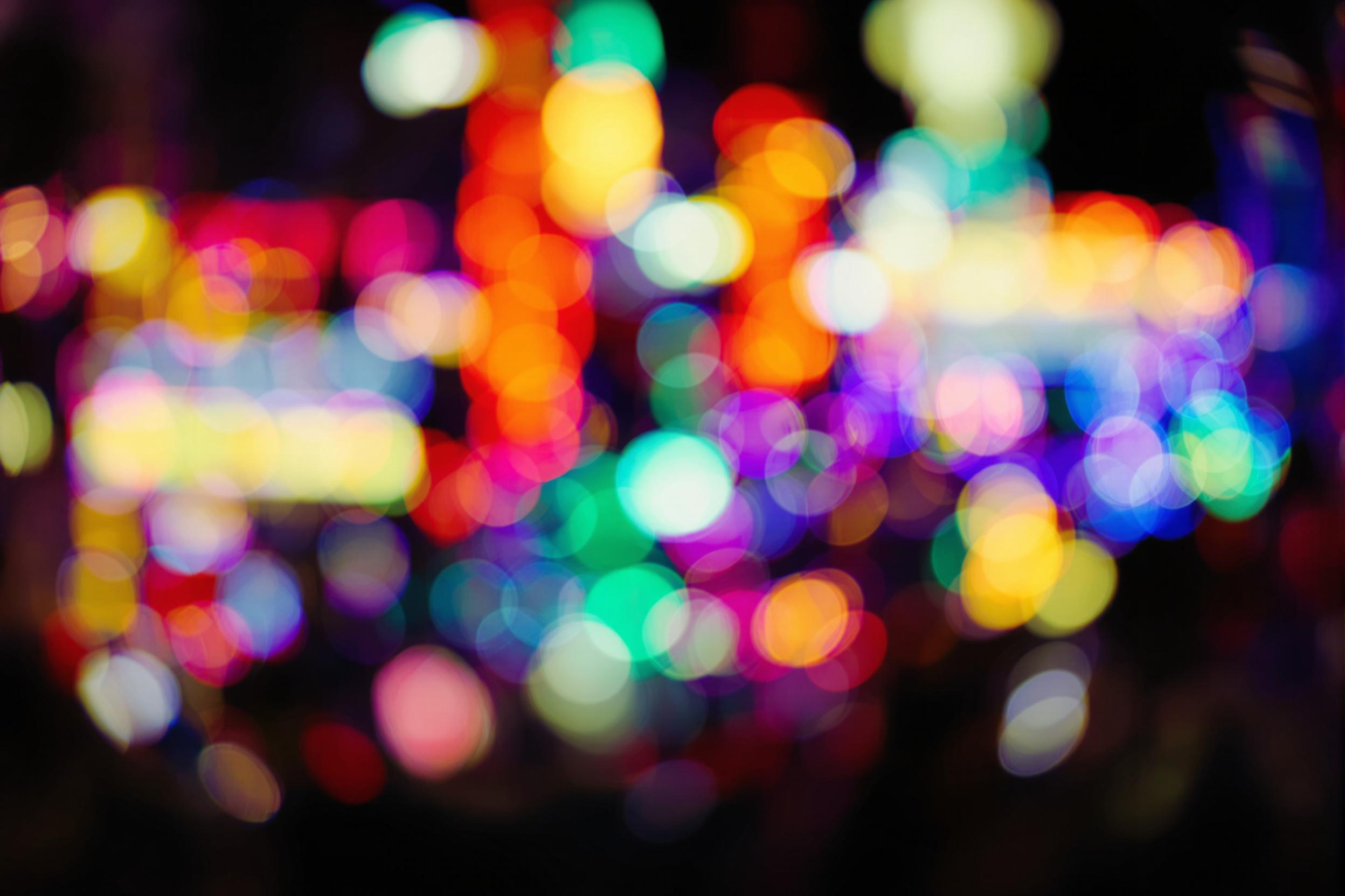 Vibrant city lights create a mesmerizing bokeh effect in this stunning nighttime urban wallpaper. Blurred neon signs and streetlights paint a colorful tapestry against a dark backdrop, perfect for those seeking a modern, atmospheric device background.