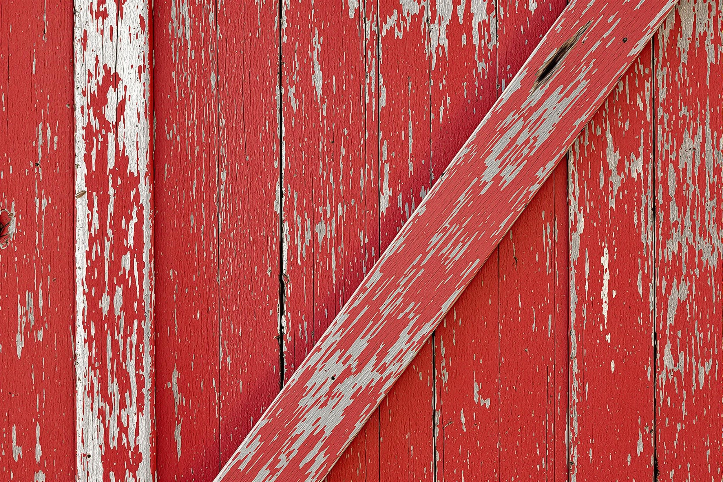 Discover the timeless beauty of rustic architecture with this close-up wallpaper of a weathered barn door. Rich wood grain patterns and faded red paint create a captivating texture, perfect for adding warmth and character to your digital devices.